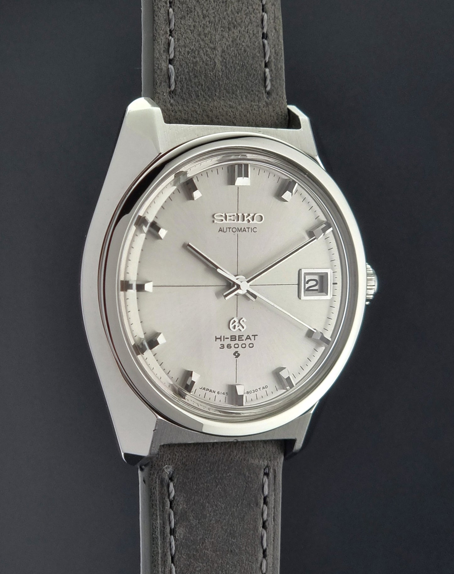 Vintage Grand Seiko watch with silver dial and gray leather strap on a dark background