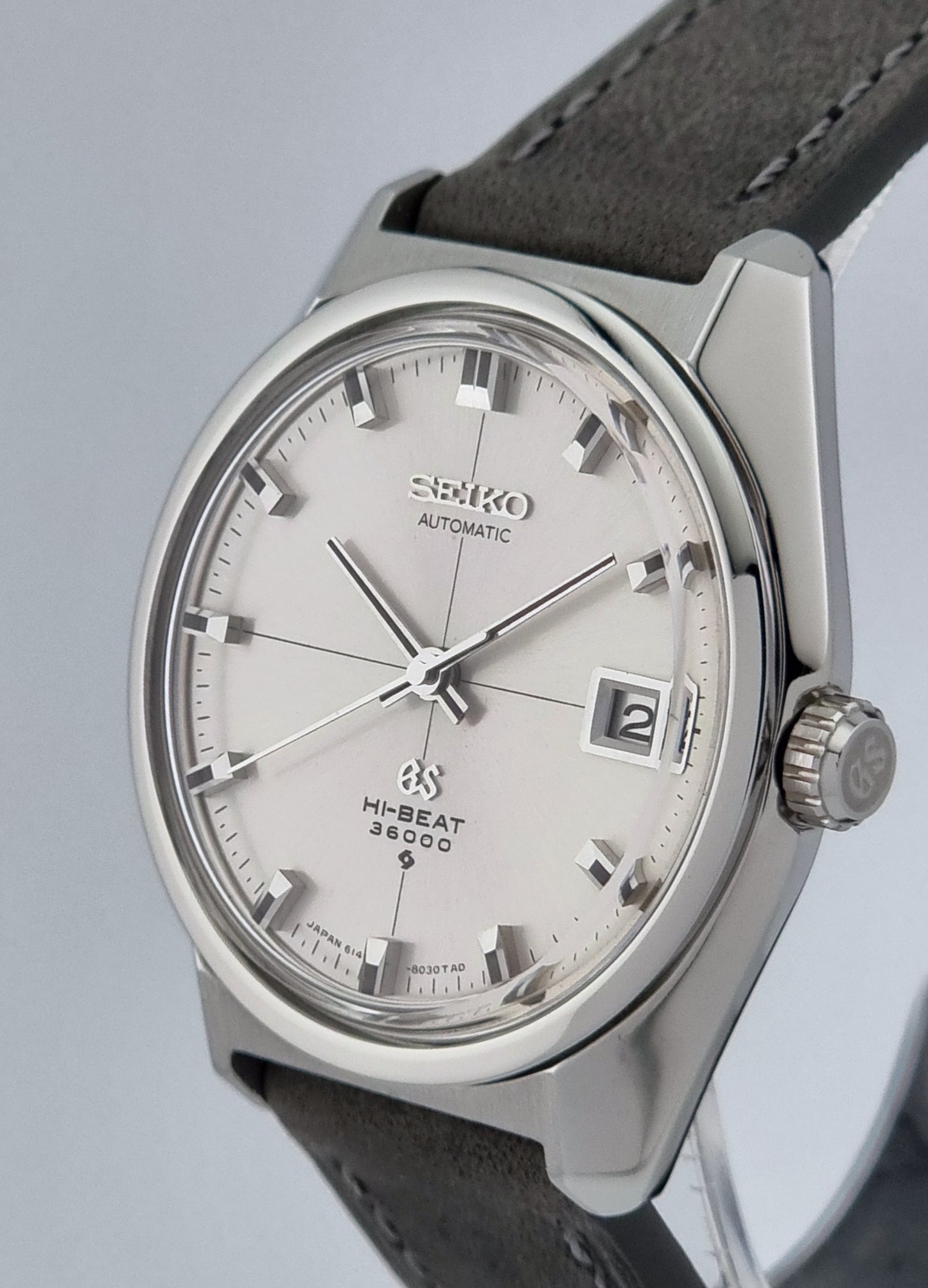Vintage Grand Seiko watch with silver dial and dark leather strap on a light gray background