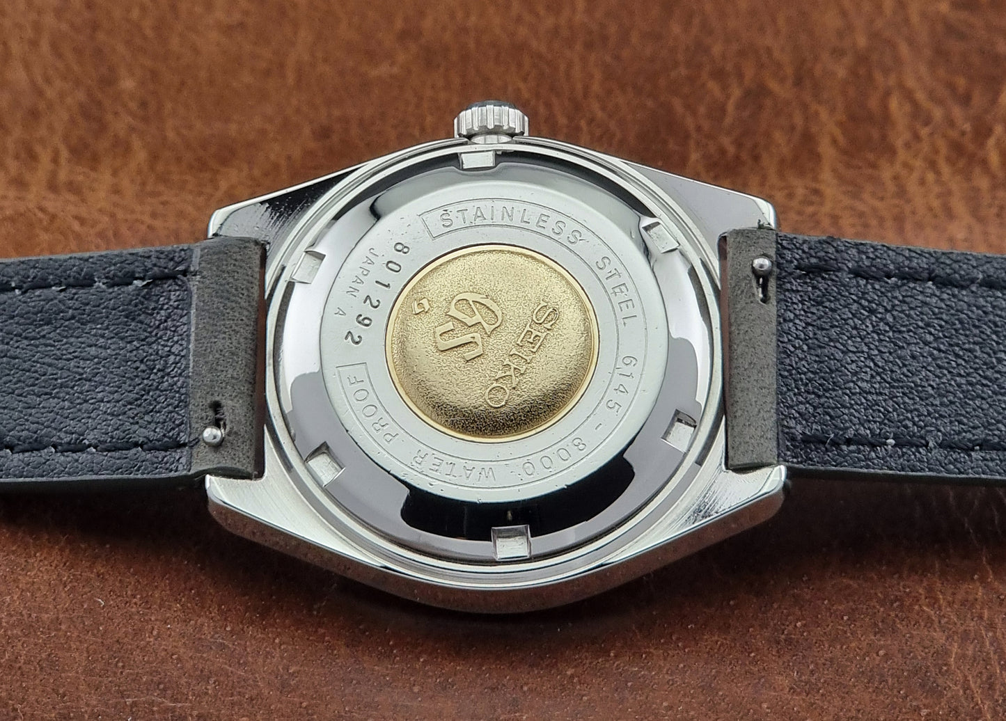 Close-up of a watch case of a Vintage Grand Seiko watch with brand logo on a brown leather background