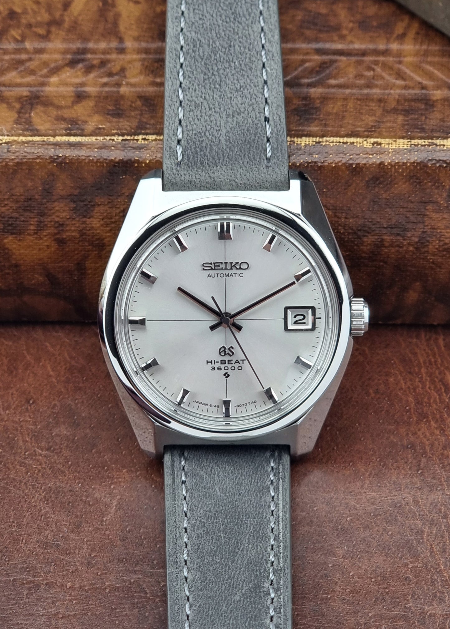 Vintage Grand Seiko watch with gray leather strap on a wooden surface