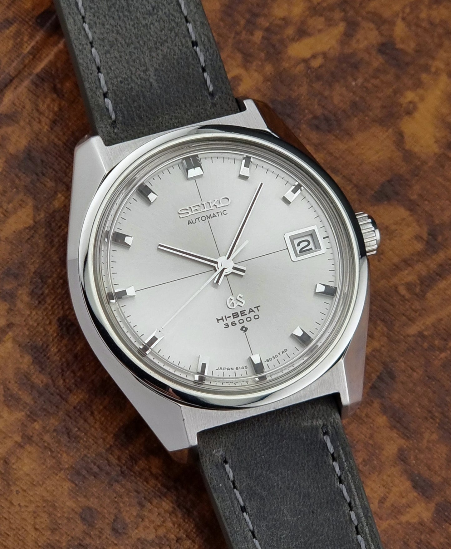 Vintage Grand Seiko watch with silver case and black leather strap on a wooden surface