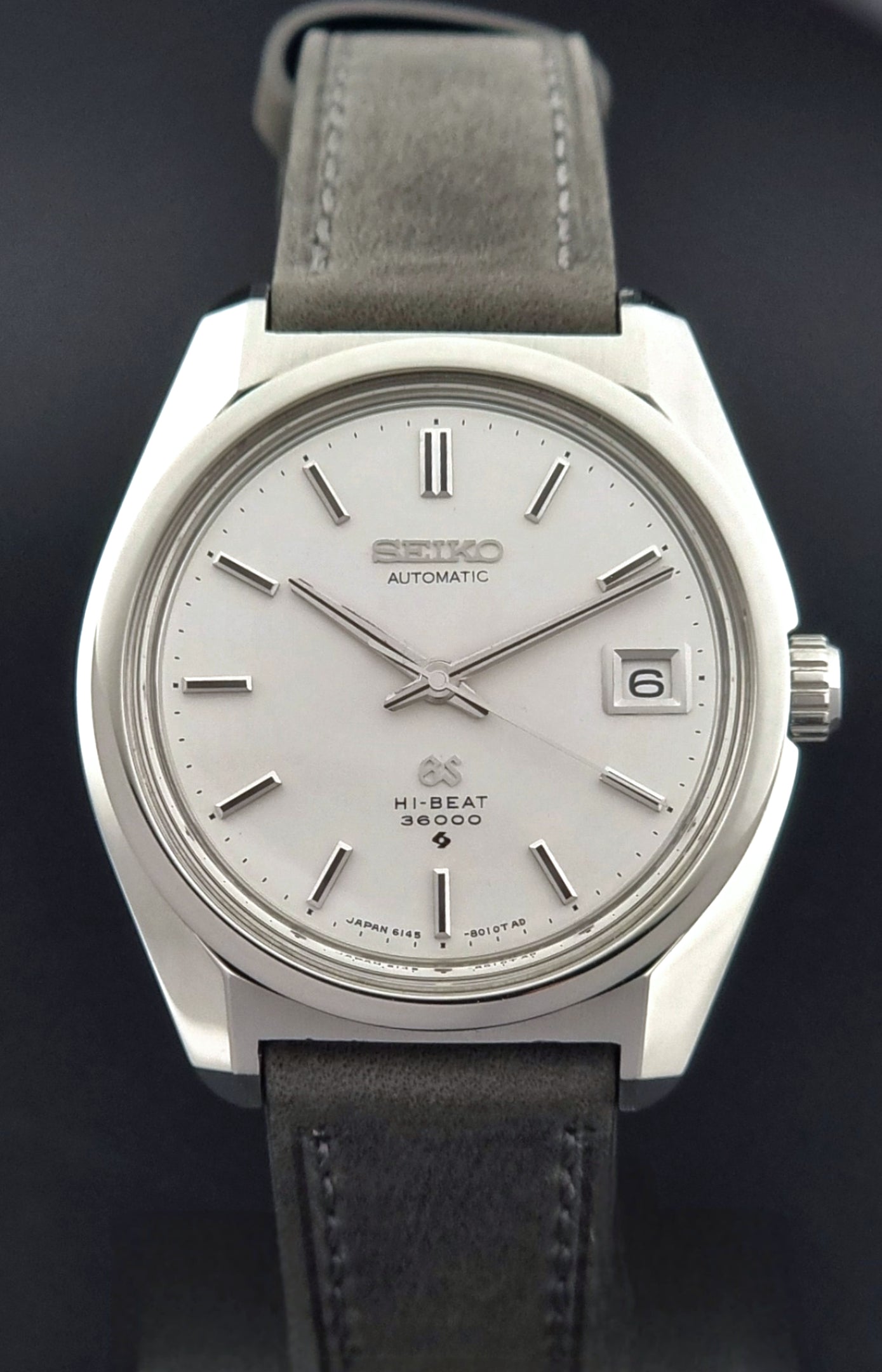 Grand Seiko 6145-8000 watch with silver dial and black leather strap on a dark background