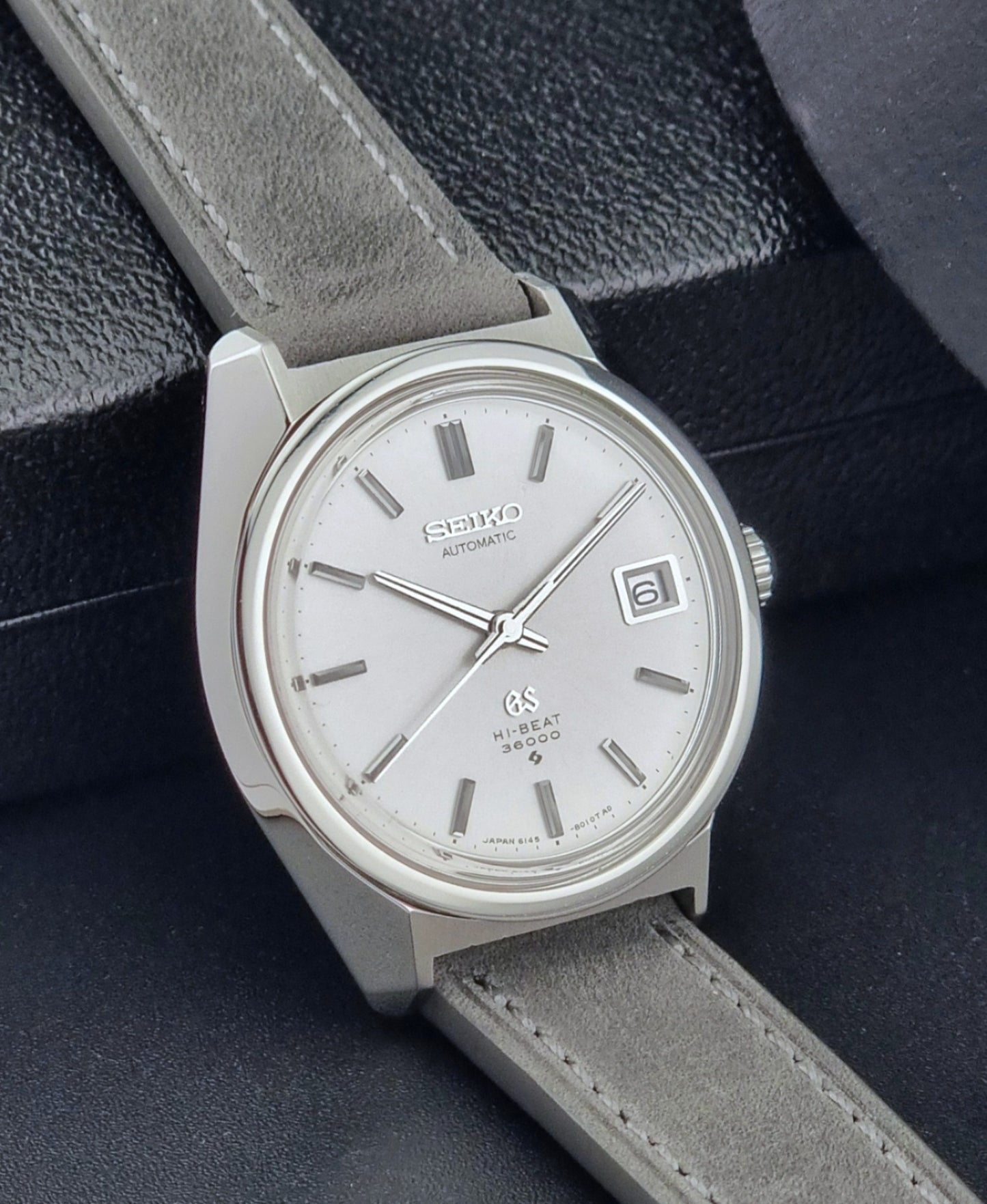 Grand Seiko 6145-8000 watch with gray strap on a dark textured background