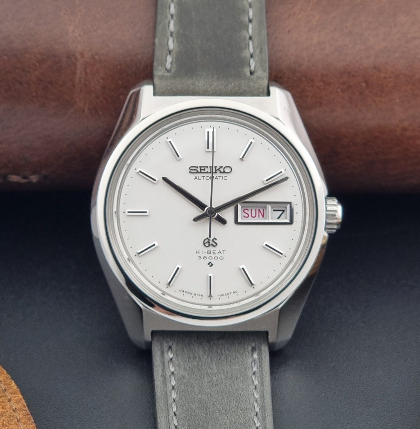 Vintage Grand Seiko Wristwatch 6146-8000 with gray strap and silver case on a dark grey background dial view
