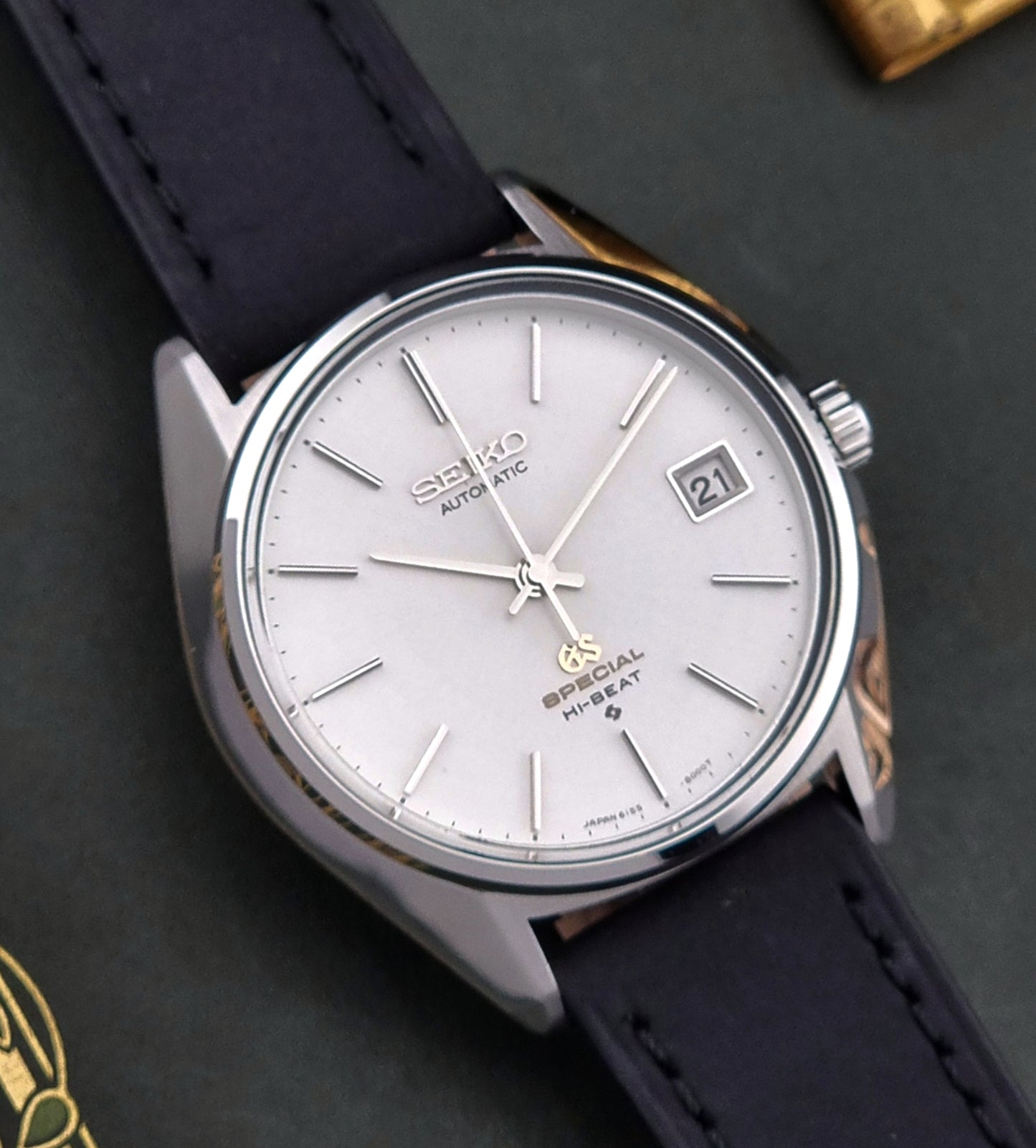 Vintage Grand Seiko Wristwatch with a white face and black leather strap on a dark background