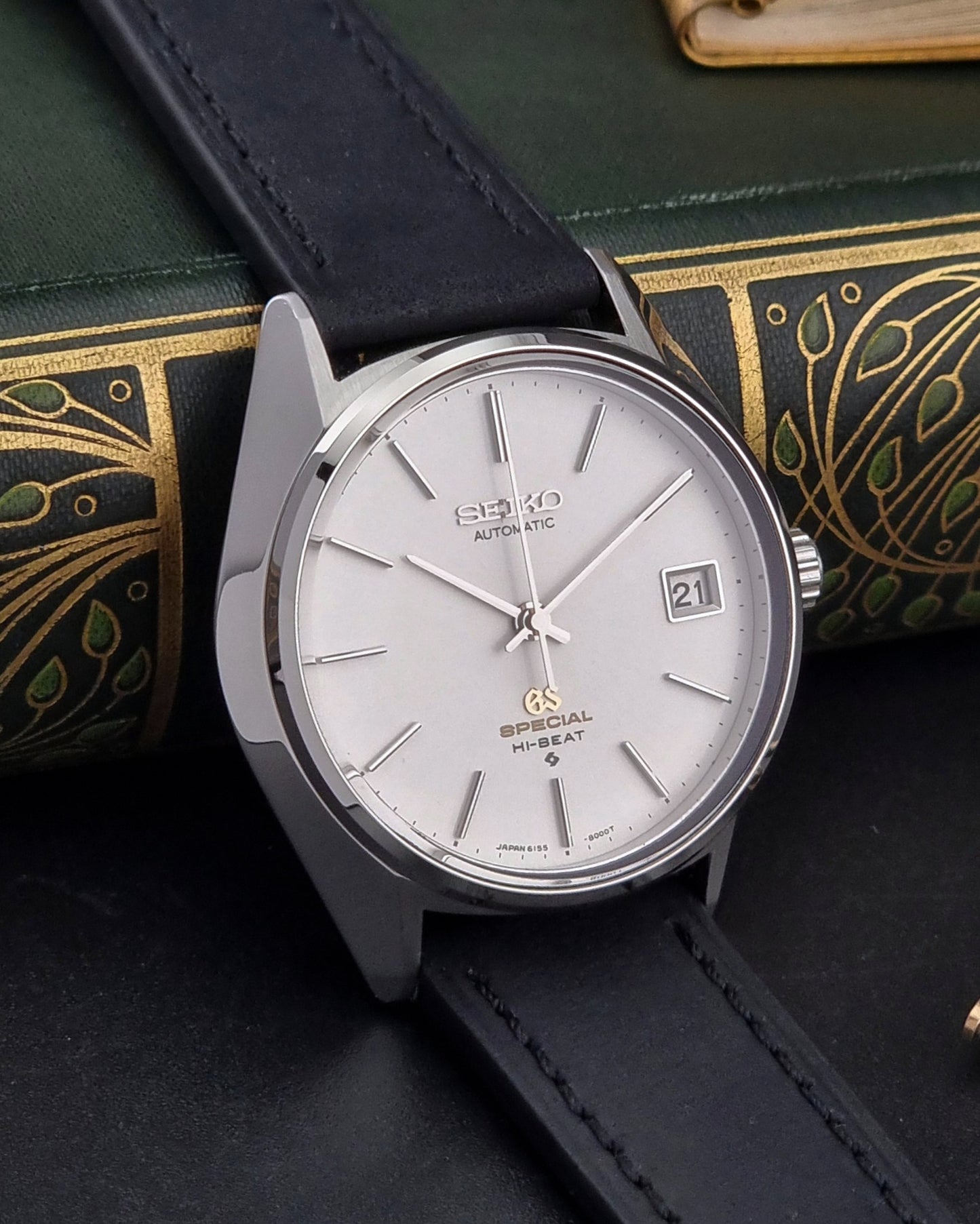 Vintage Grand Seiko watch with black leather strap on a decorative book