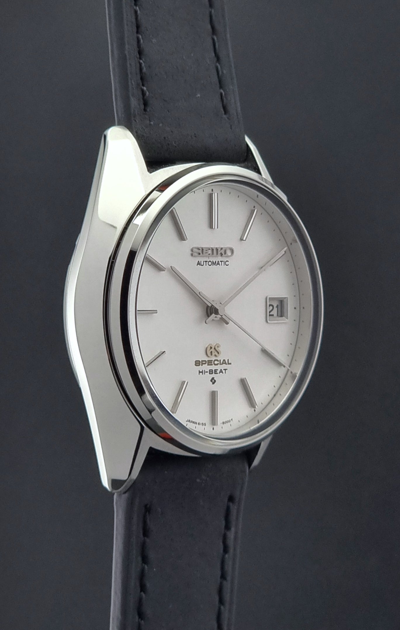Vintage Grand Seiko Wristwatch with silver case and black leather strap on a dark background