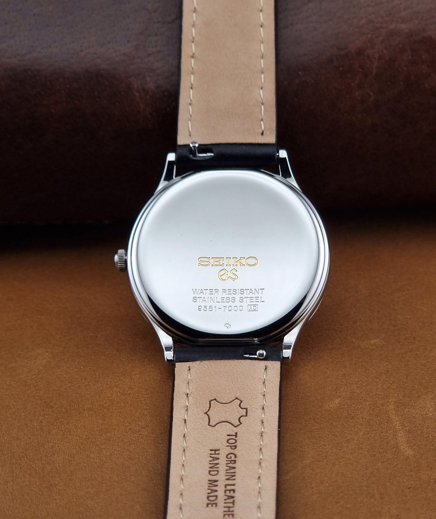 Vintage Grand Seiko 9581-7000 Quartz with black strap and silver case on a brown background case back view