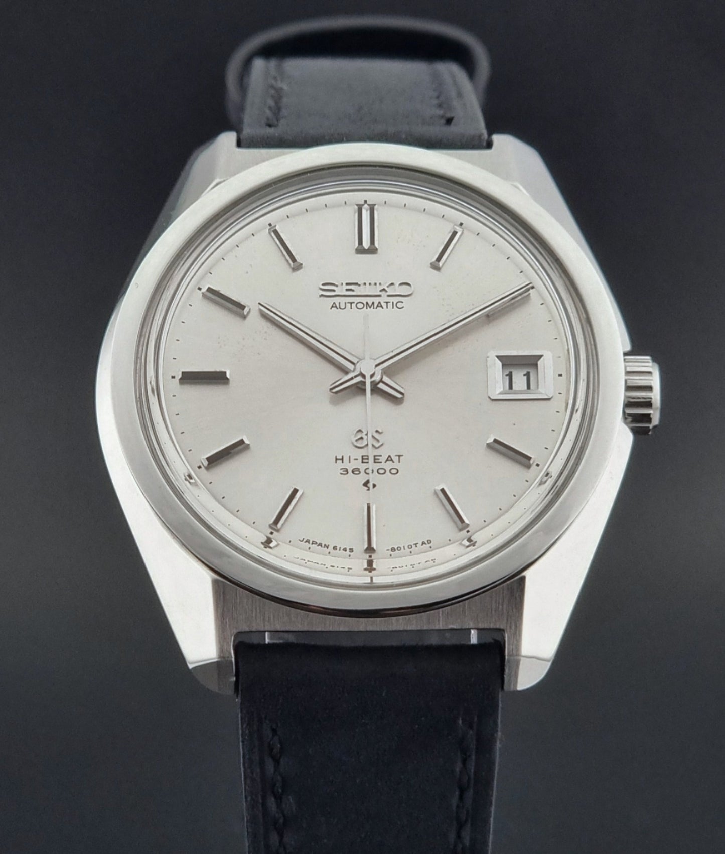 Vintage watch with black leather strap and silver case on a dark background