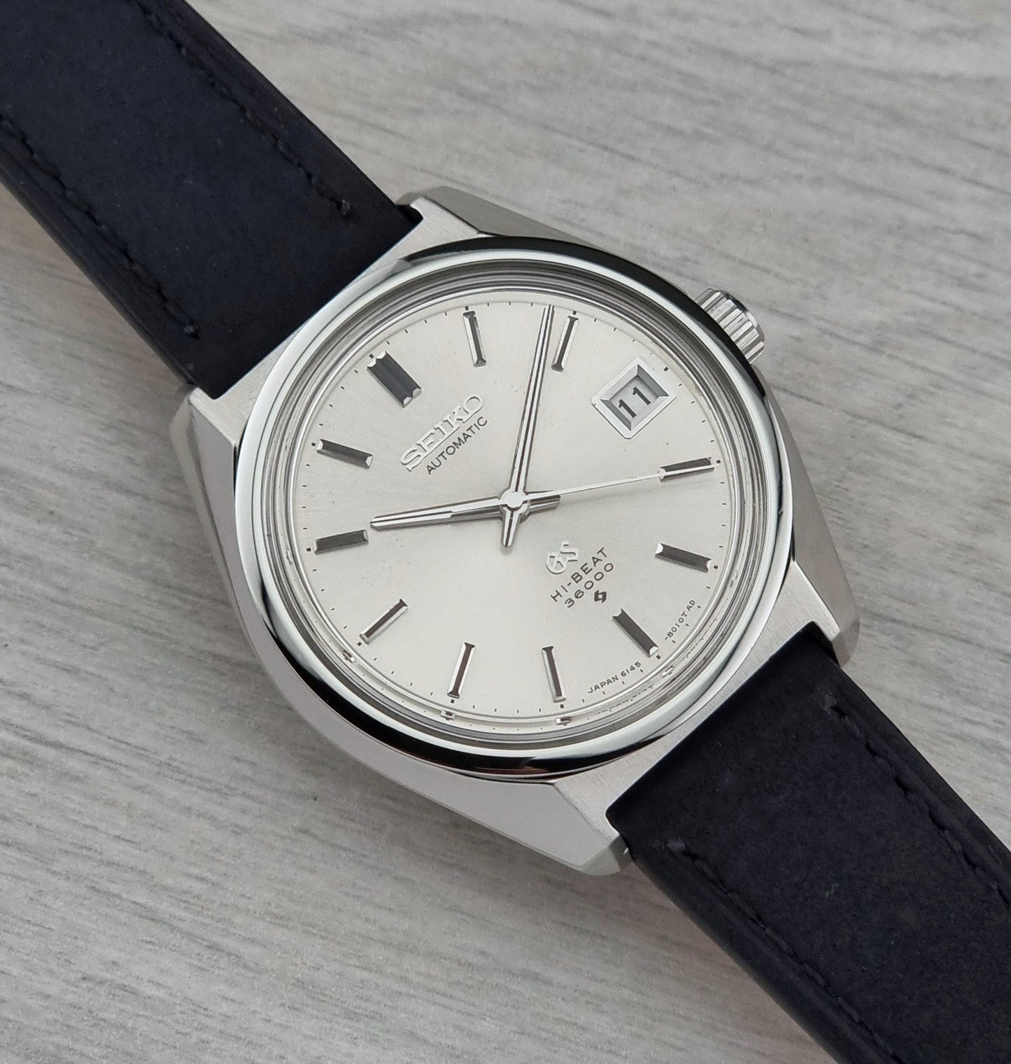 Vintage-style watch with black leather strap and silver case on a light gray background