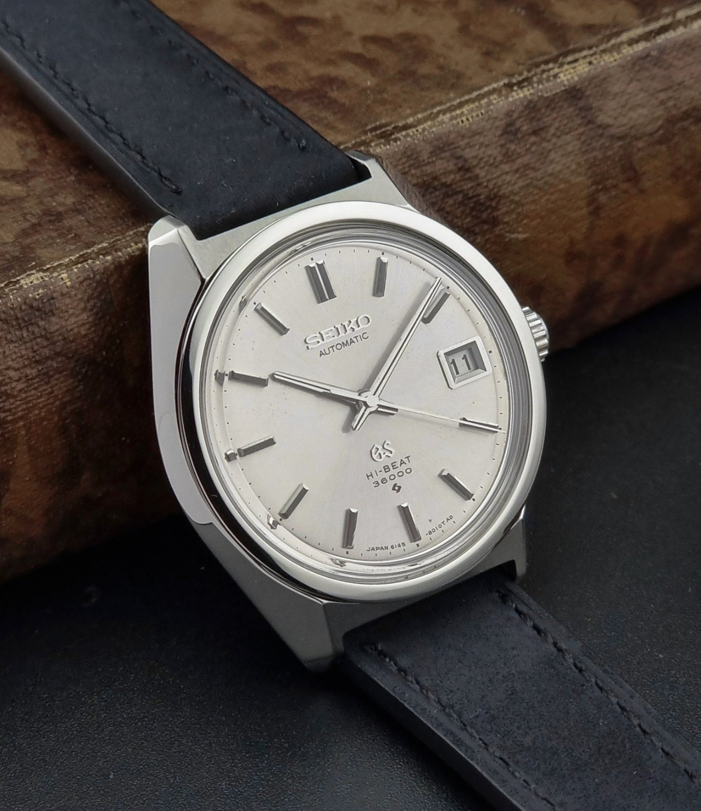 Silver Seiko watch with black leather strap on a wooden surface
