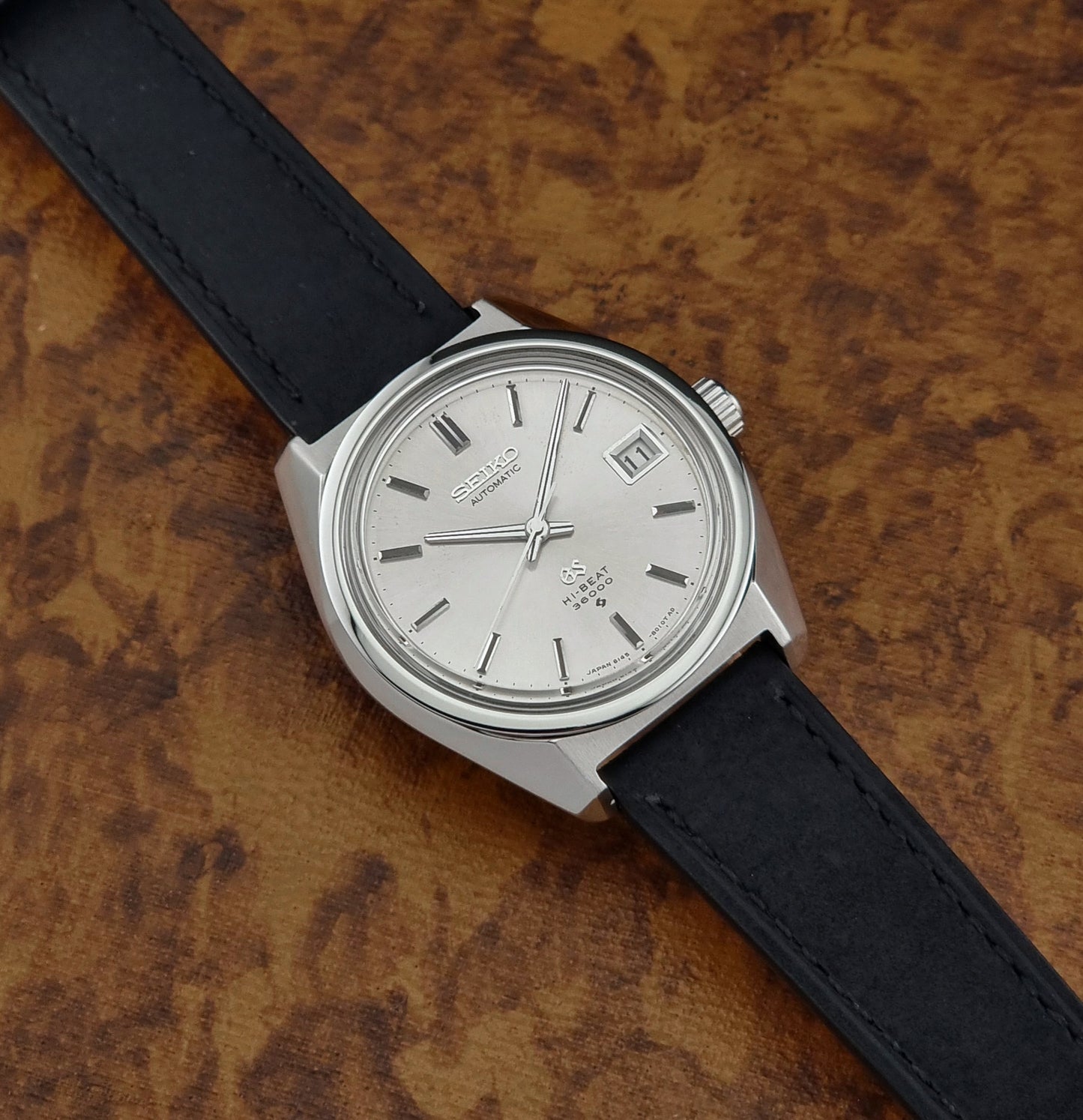 Wristwatch with black strap and silver case on a textured brown background