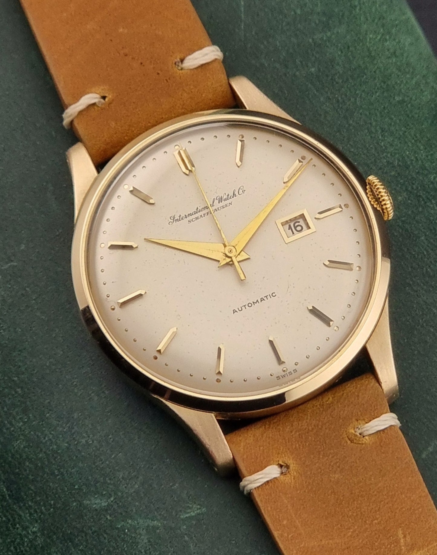 Vintage IWC watch with gold casing and brown leather strap on a green background