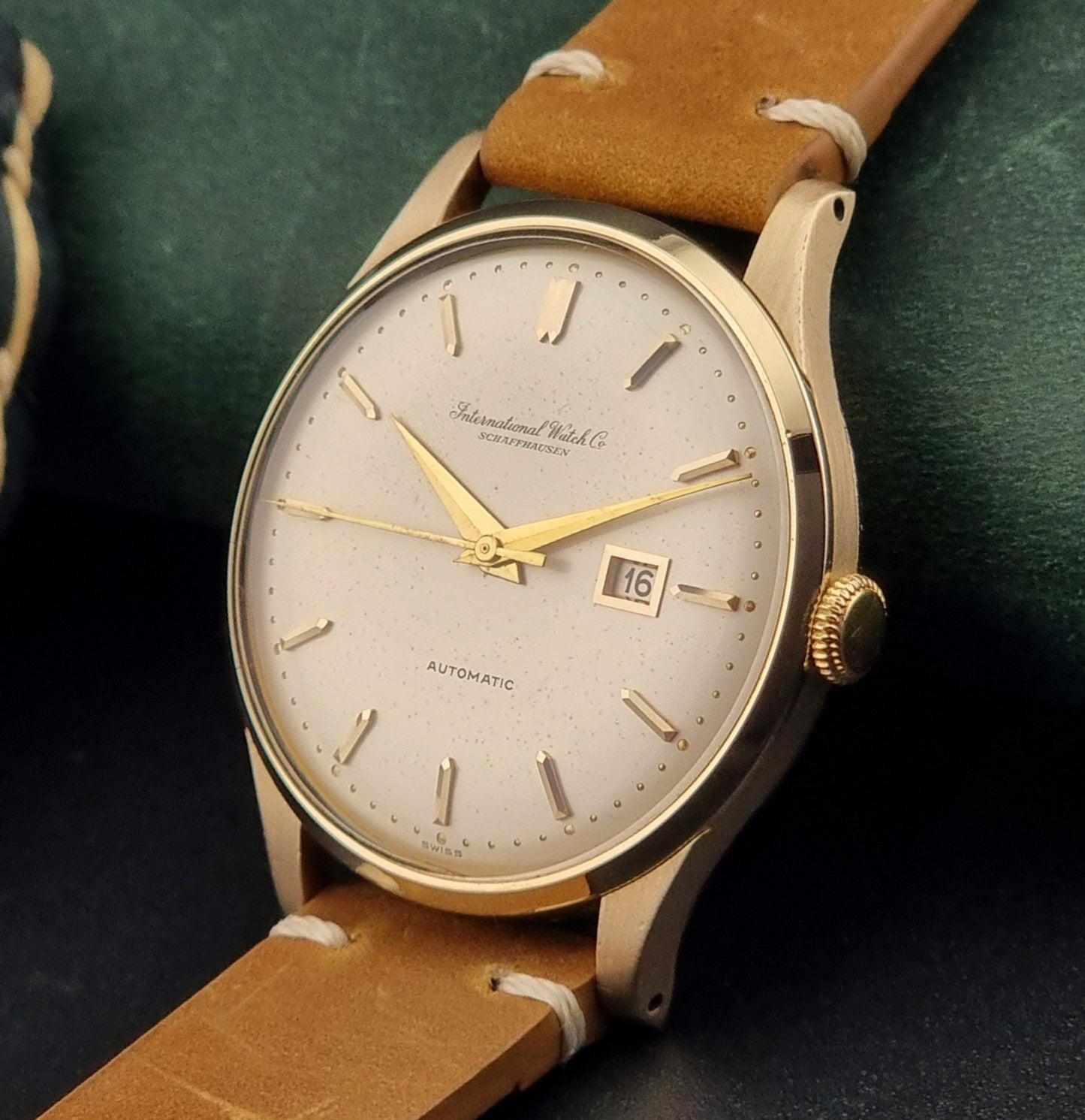 A vintage gold-plated IWC watch with a champagne dial, manual winding, and a brown leather strap