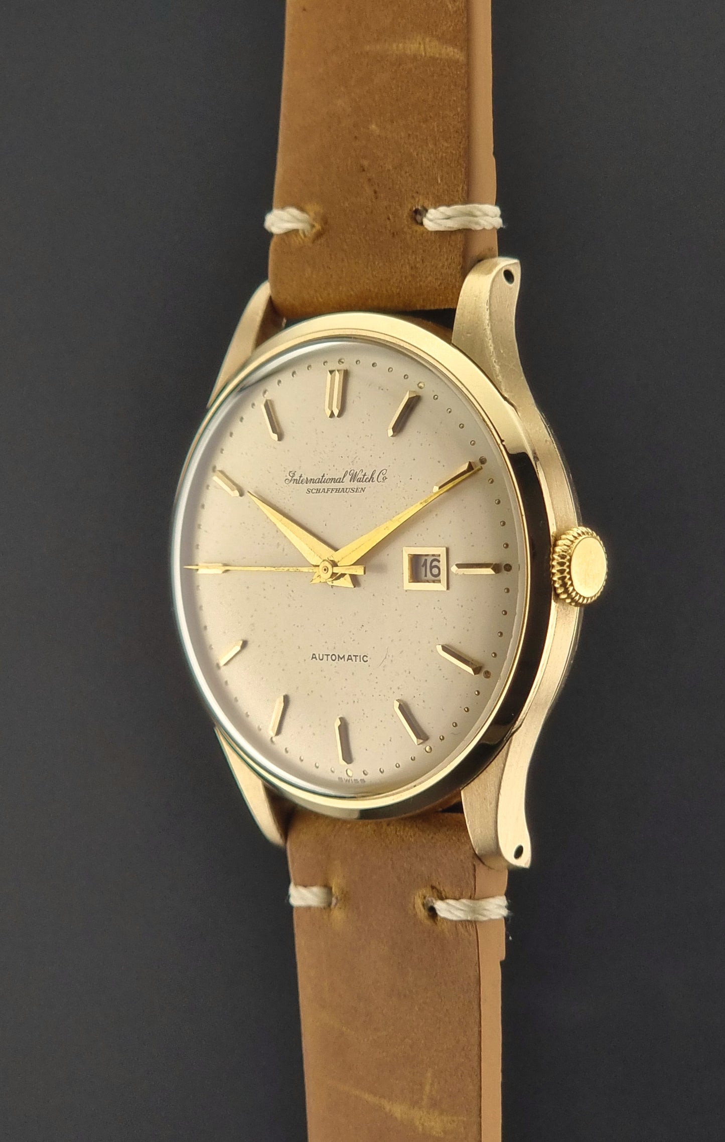 A vintage gold-plated IWC watch with a champagne dial, manual winding, and a brown leather strap