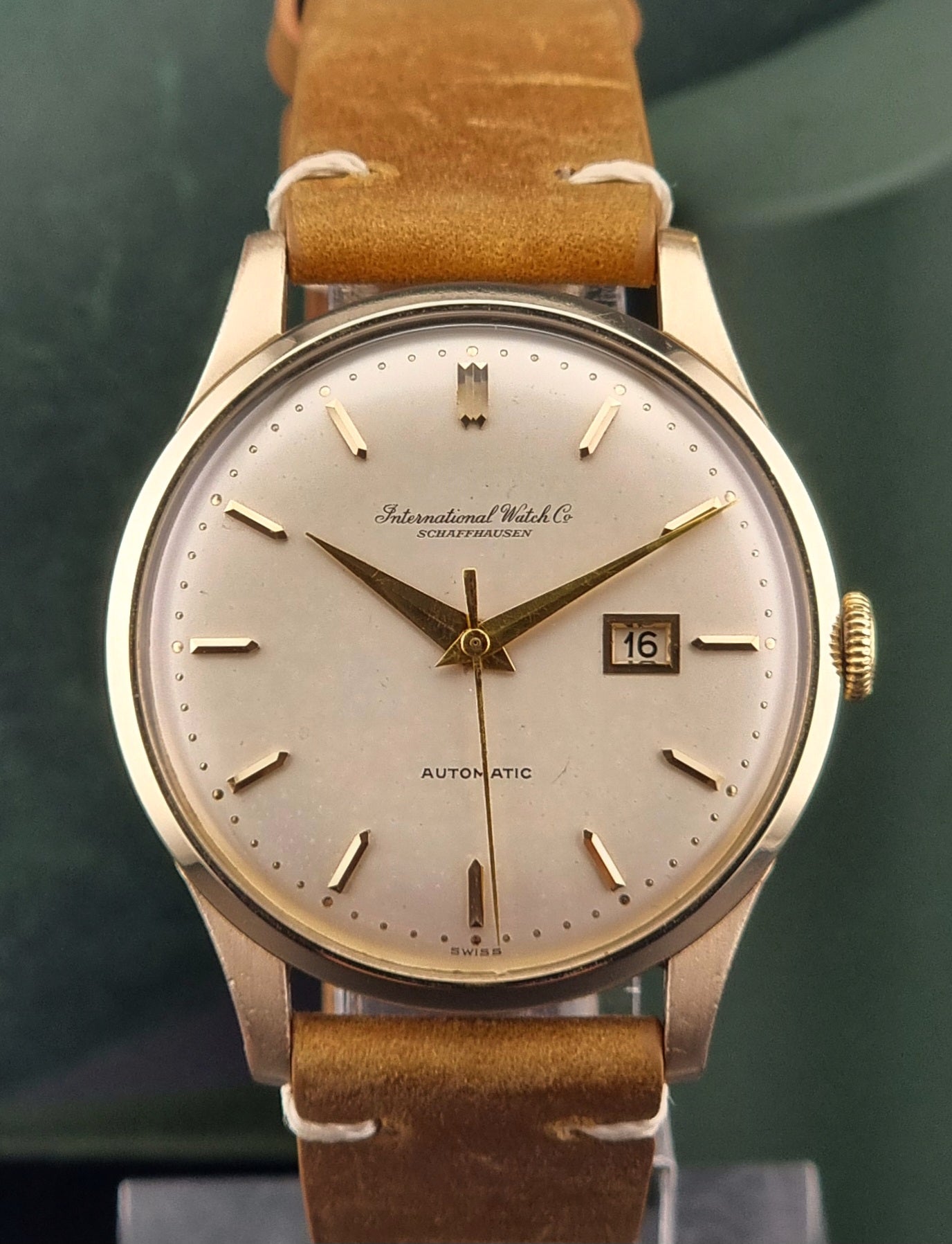 A vintage gold-plated IWC watch with a champagne dial, manual winding, and a brown leather strap