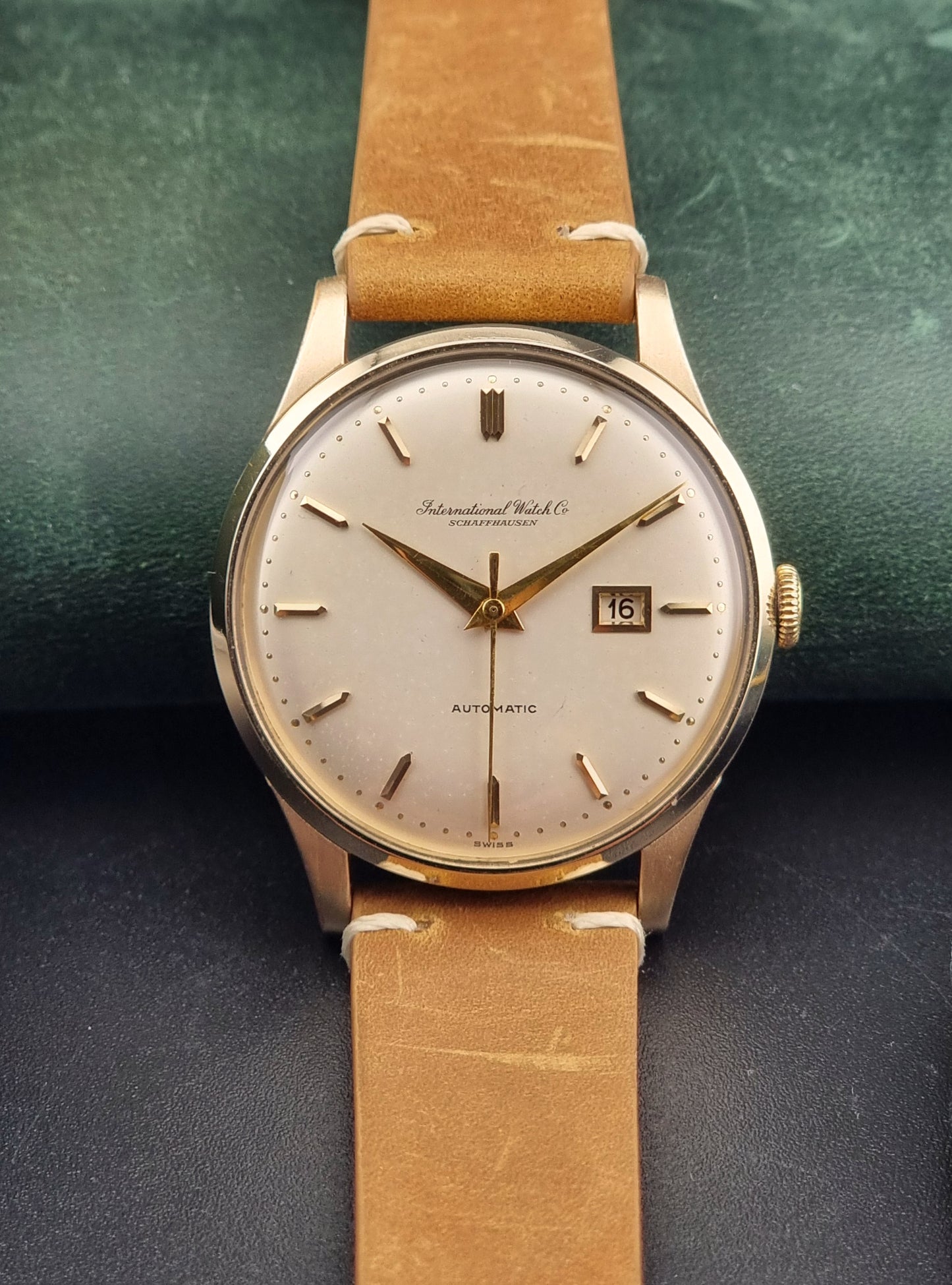 A vintage gold-plated IWC watch with a champagne dial, manual winding, and a brown leather strap