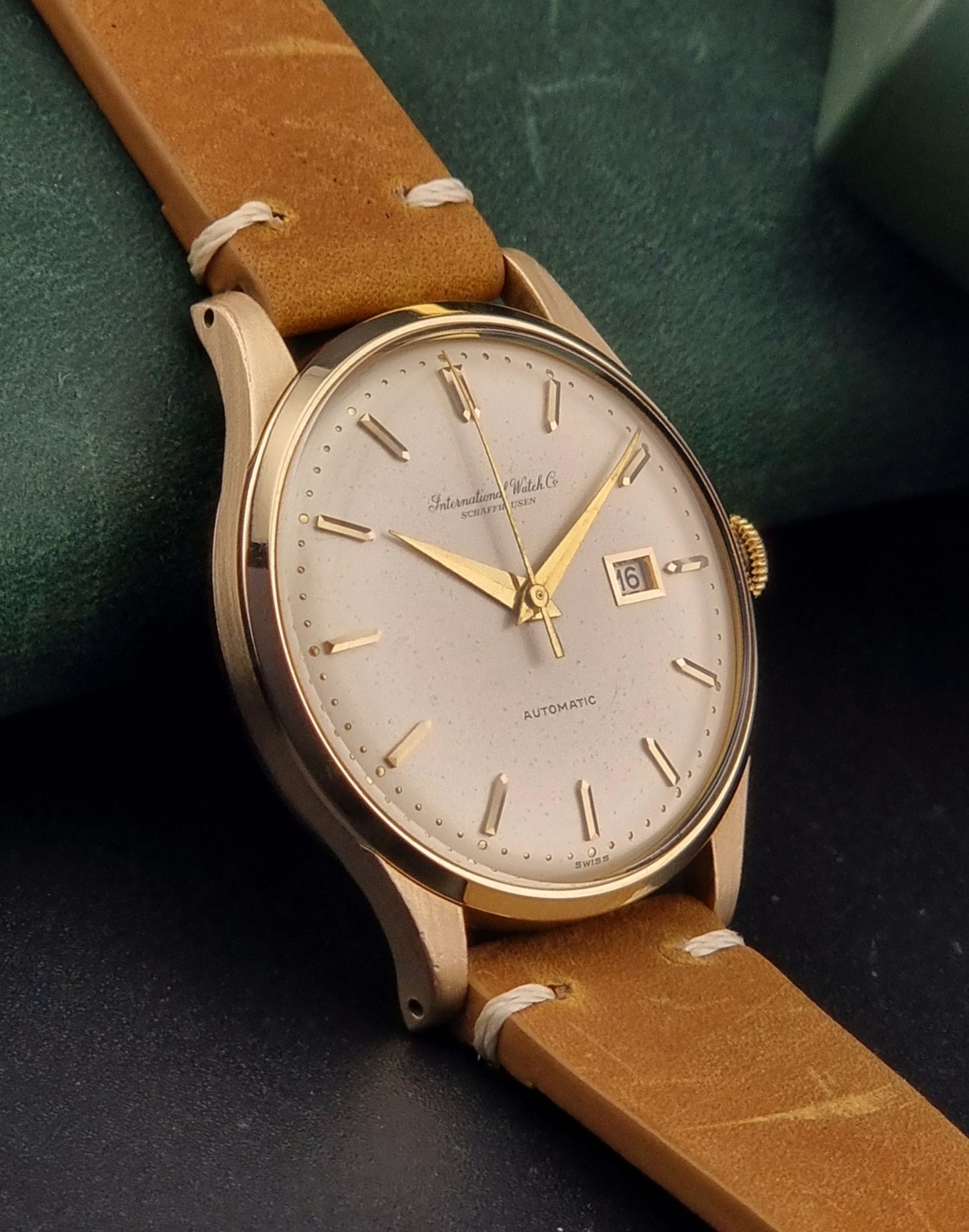 A vintage gold-plated IWC watch with a champagne dial, manual winding, and a brown leather strap