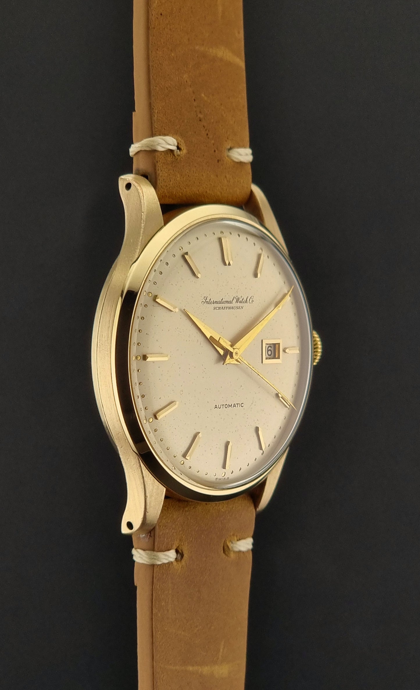 A vintage gold-plated IWC watch with a champagne dial, manual winding, and a brown leather strap