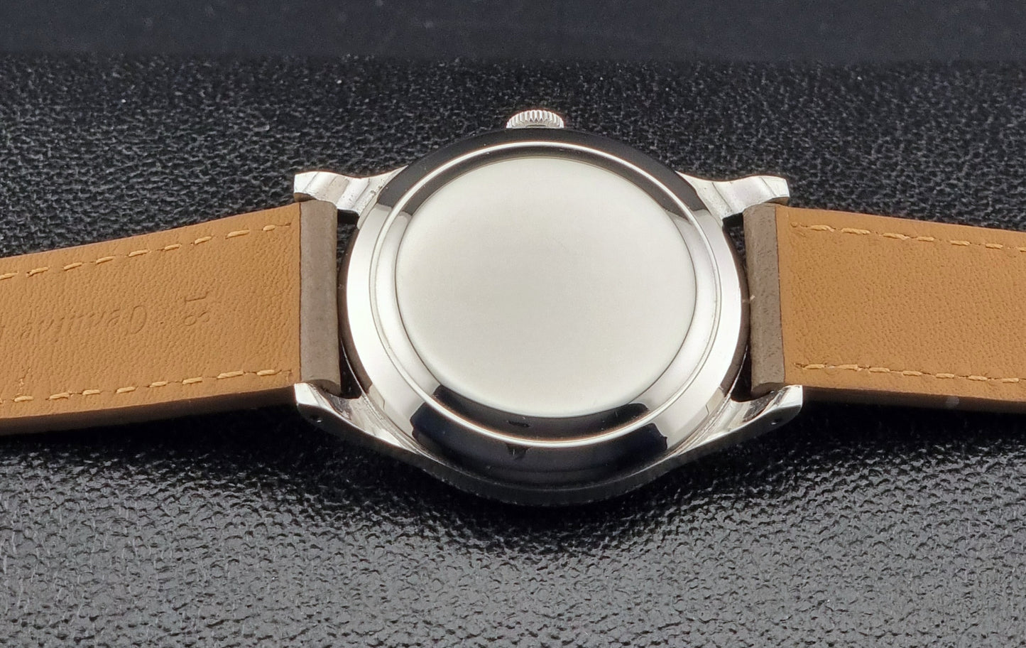 Vintage IWC Wristwatch case back with a brown leather strap on a dark textured background