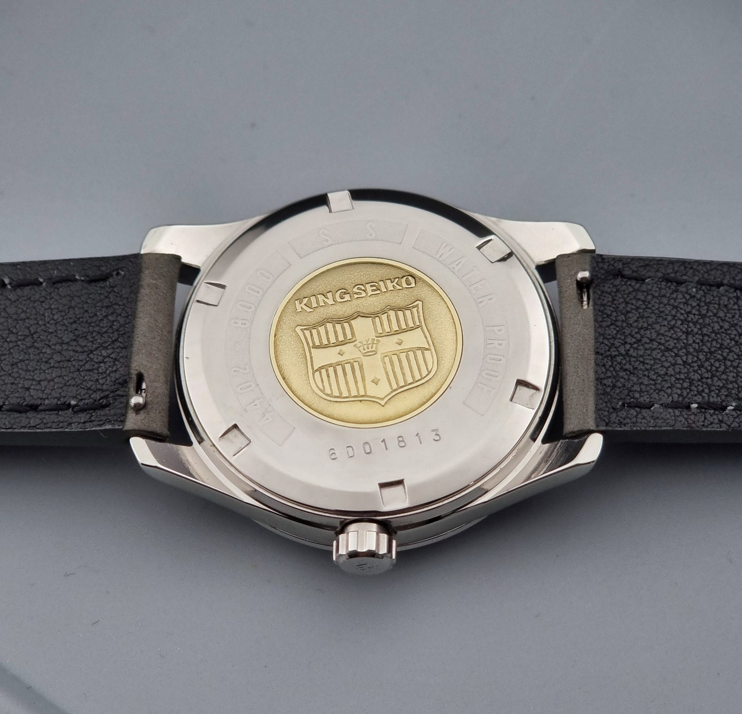 Vintage King Seiko 4402-8000 watch with a silver case and grey leather strap on a gray background case back view