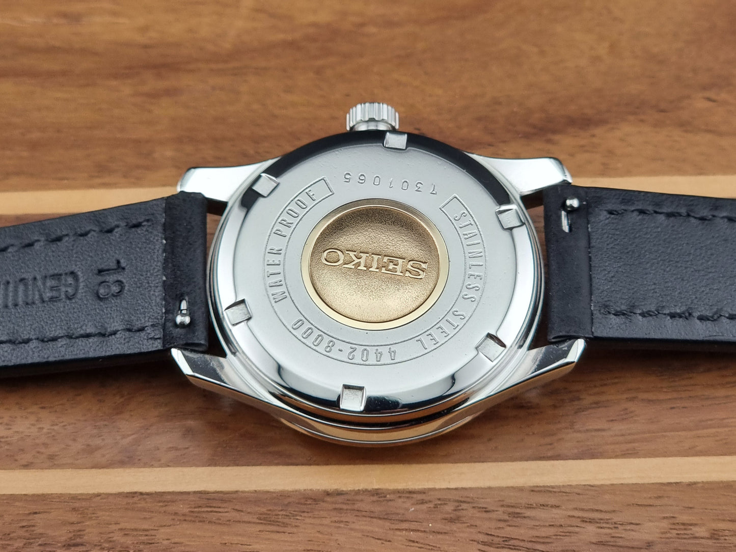 Vintage King Seiko 4402-8000 case back with black leather strap and visible brand logo on wooden surface