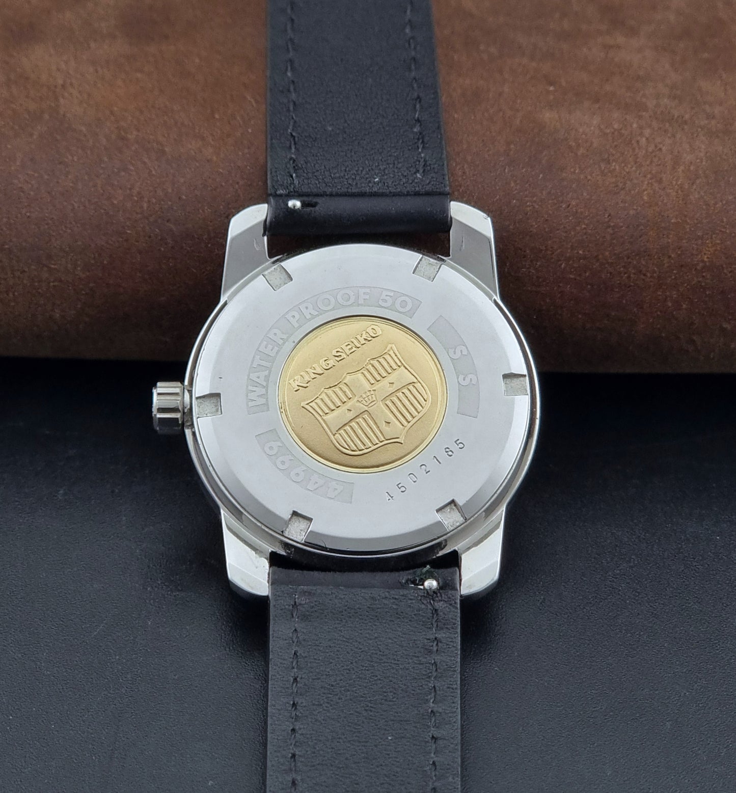 Vintage King Seiko Wristwatch 44999 with a black leather strap on a dark surface case back view