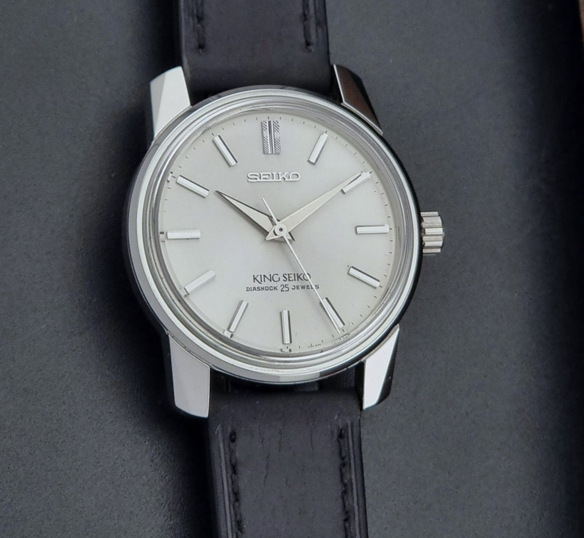 Vintage King Seiko Wristwatch 44999 with a black leather strap on a dark surface front view