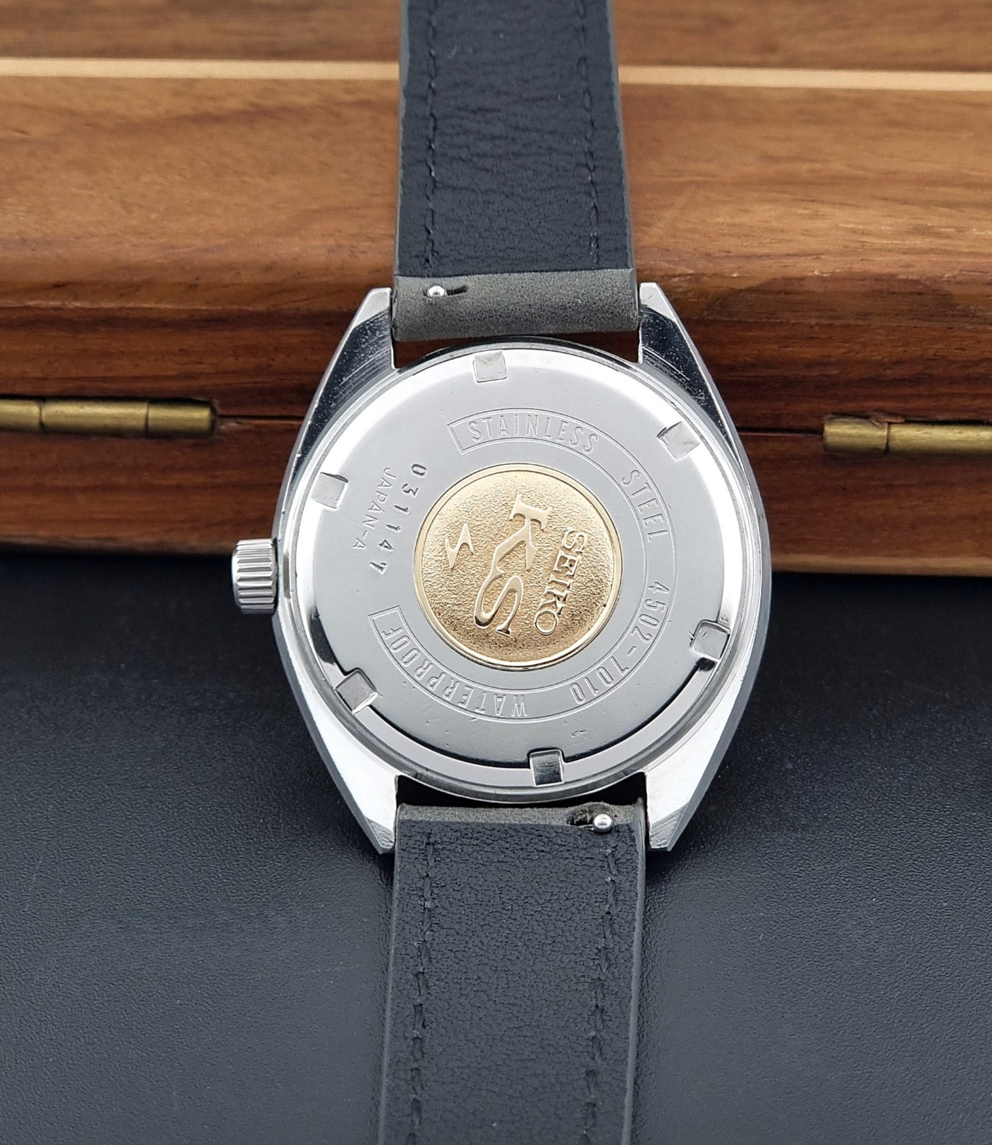 Vintage King Seiko Wristwatch 4502-7010 with gray strap and silver case on a wooden surface case back view