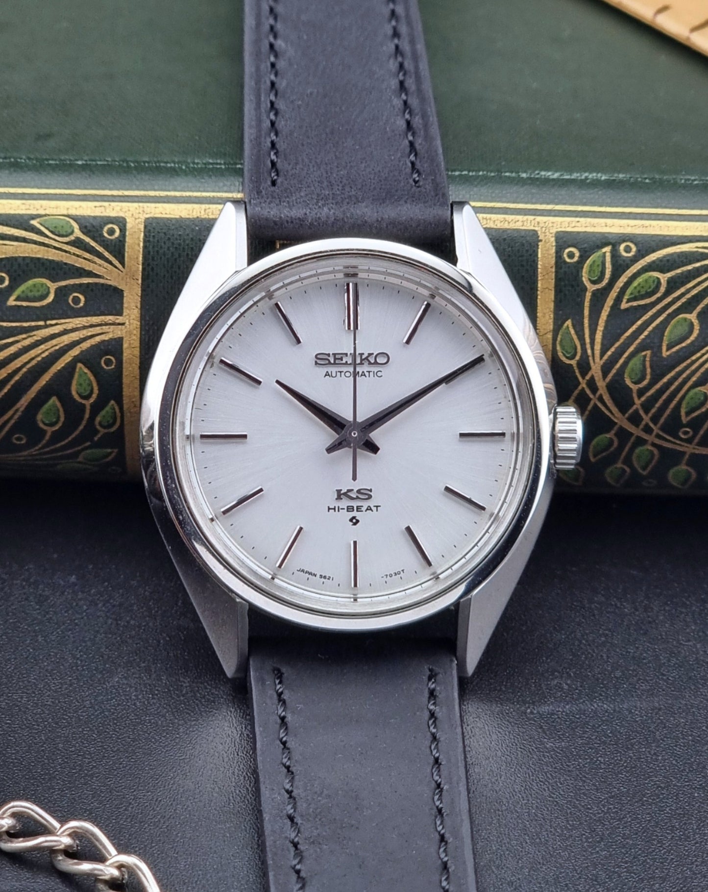 King Seiko watch with a white face and dark leather strap on a decorative surface