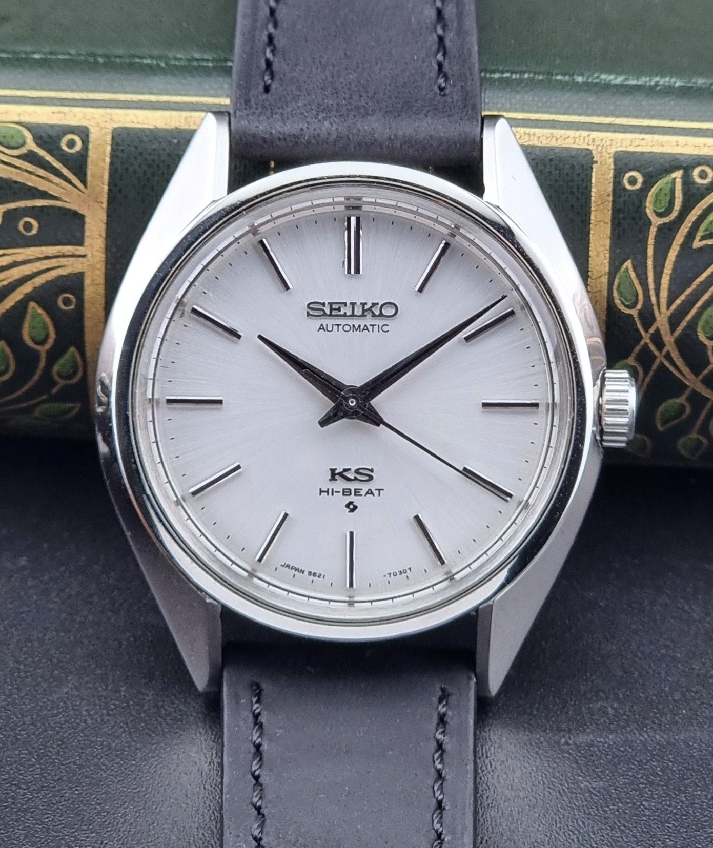 King Seiko watch with a silver case and dark leather strap on a decorative background