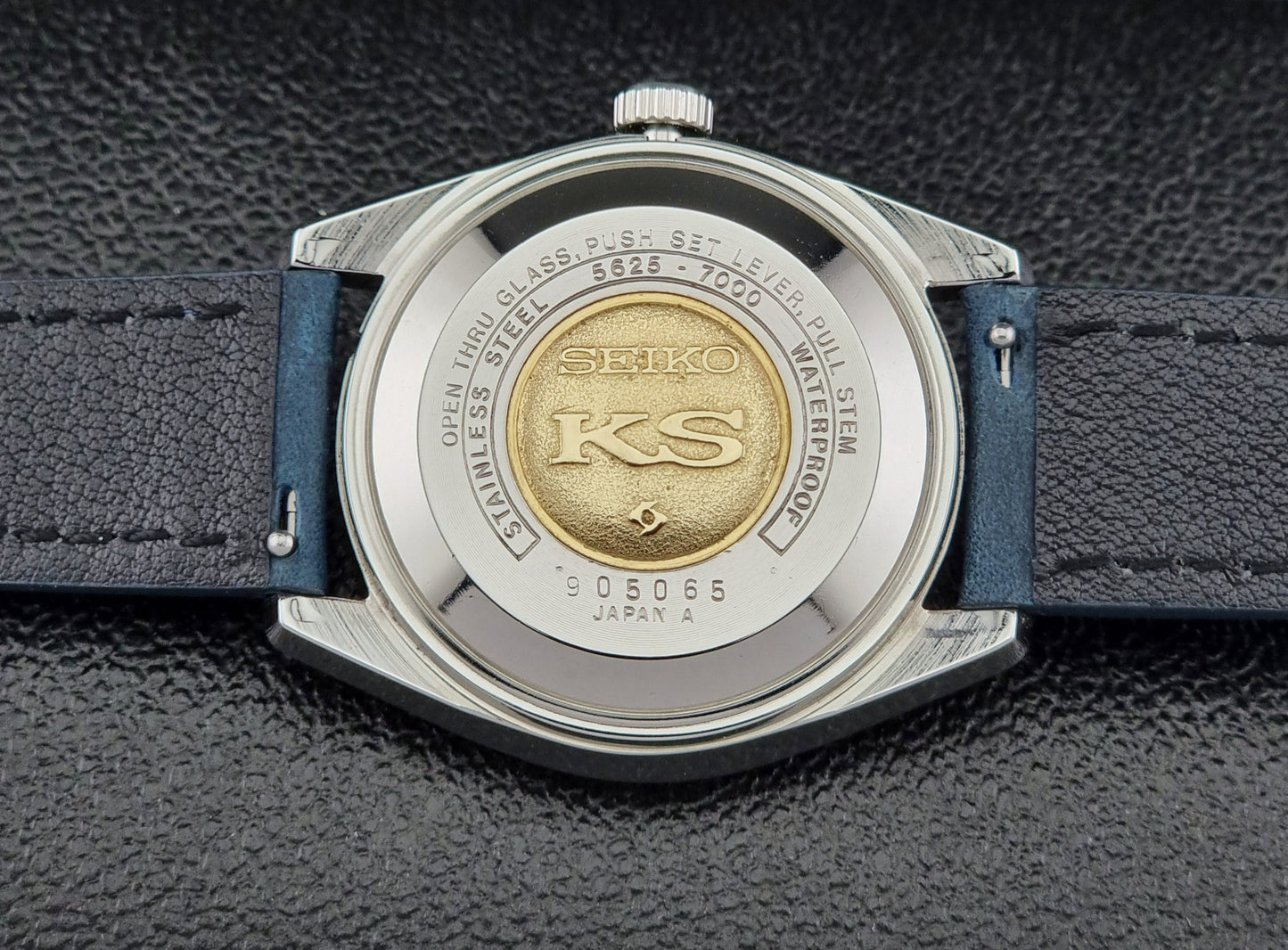 Vintage King Seiko 5625-7000 Wristwatch case back with blue strap and silver case on a dark textured background
