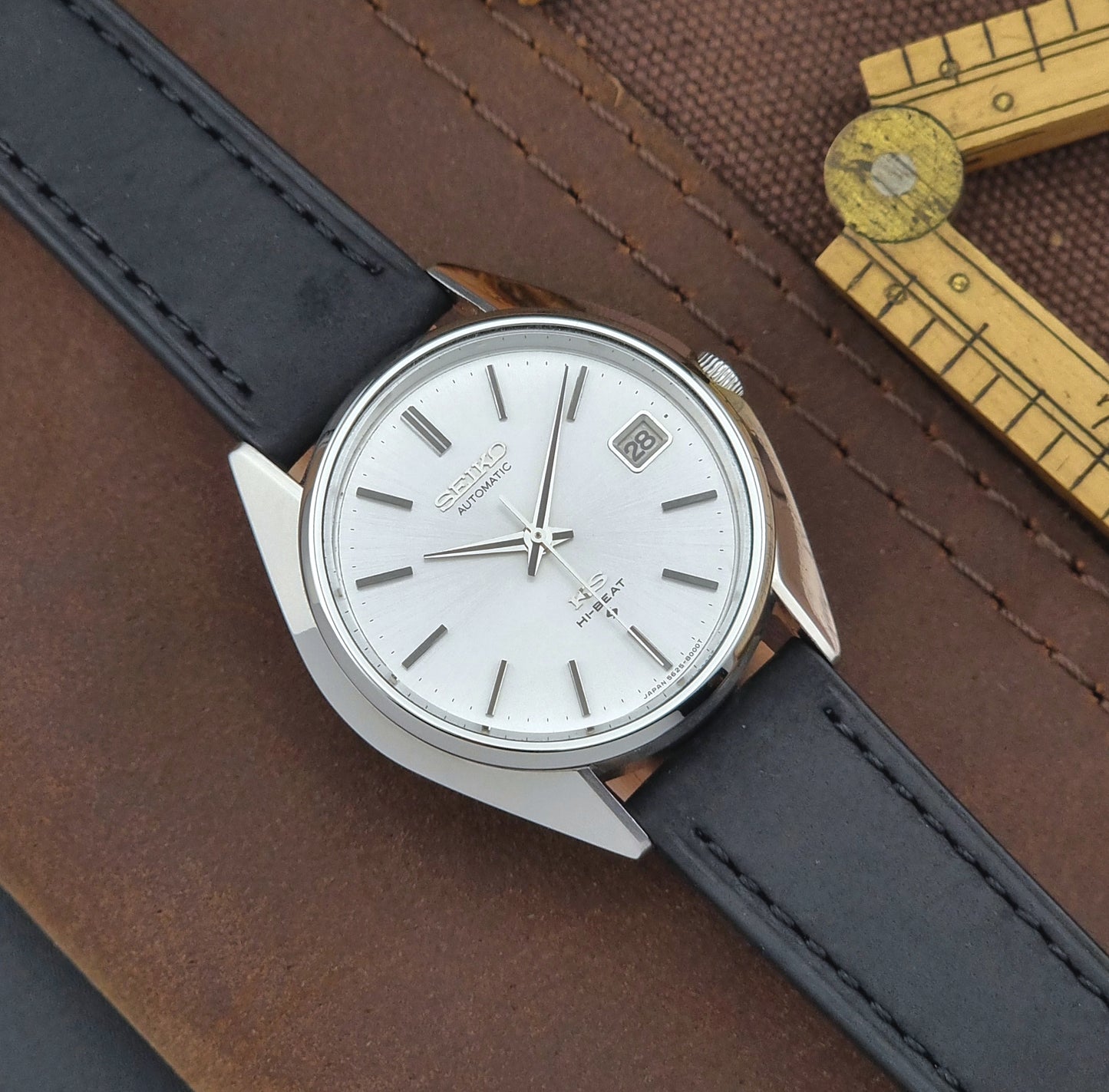 Vintage King Seiko Wristwatch with black leather strap and silver case on a brown textured background