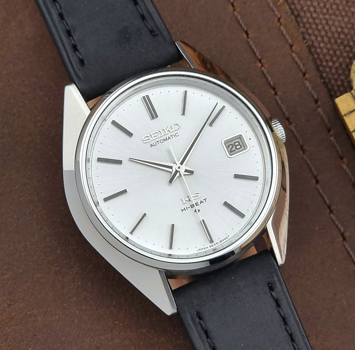 Vintage King Seiko watch with black leather strap on a brown textured background