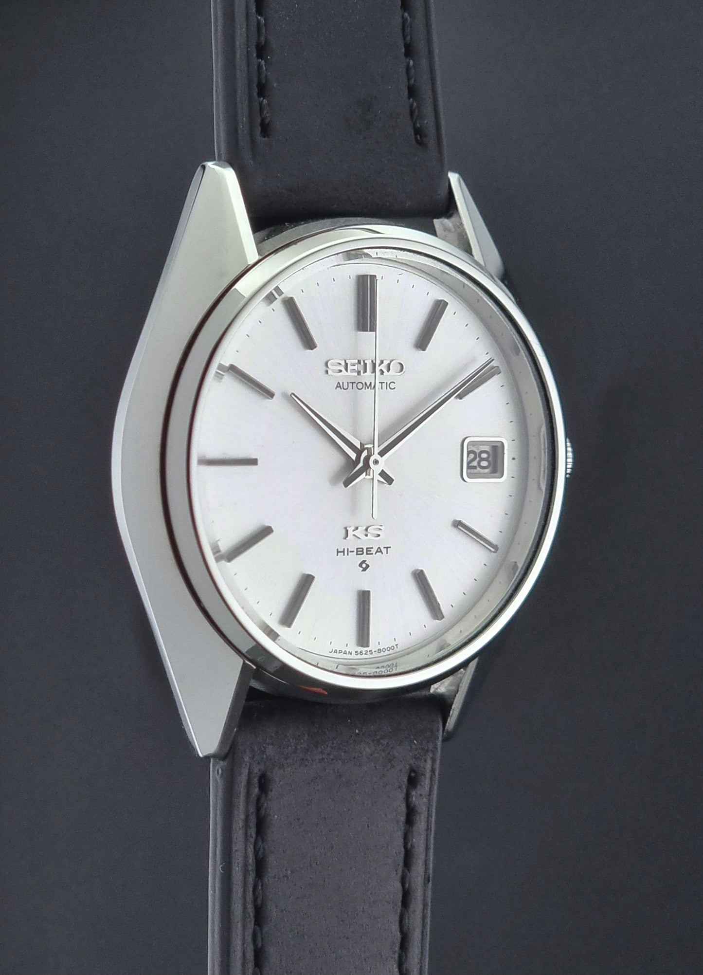 Vintage King Seiko watch with silver dial and black leather strap on a dark background