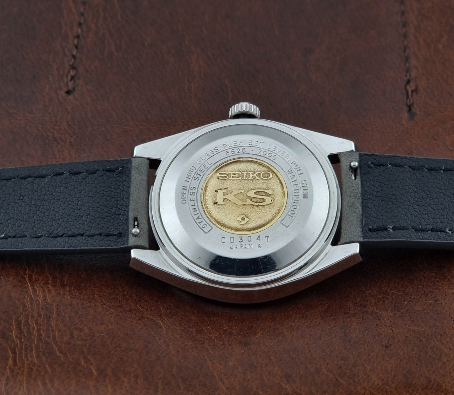 Vintage King Seiko wristwatch with gray leather strap on a brown background case back view