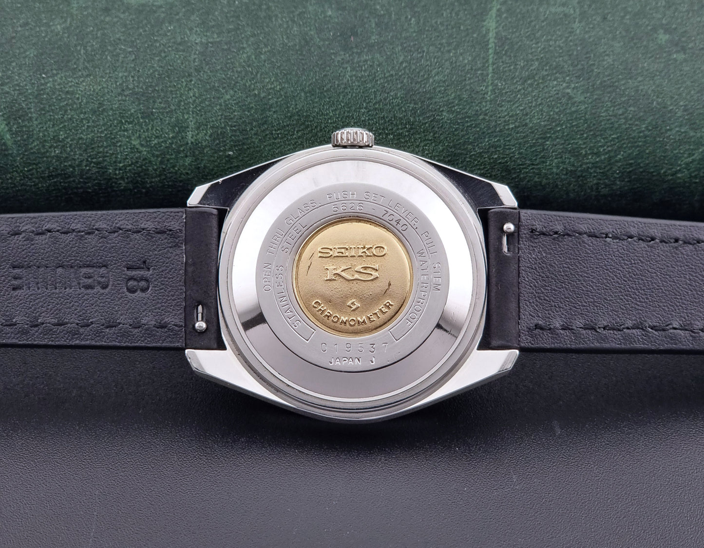 King Seiko watch 5626-7040 watch with black leather strap on a green and gray background case back view