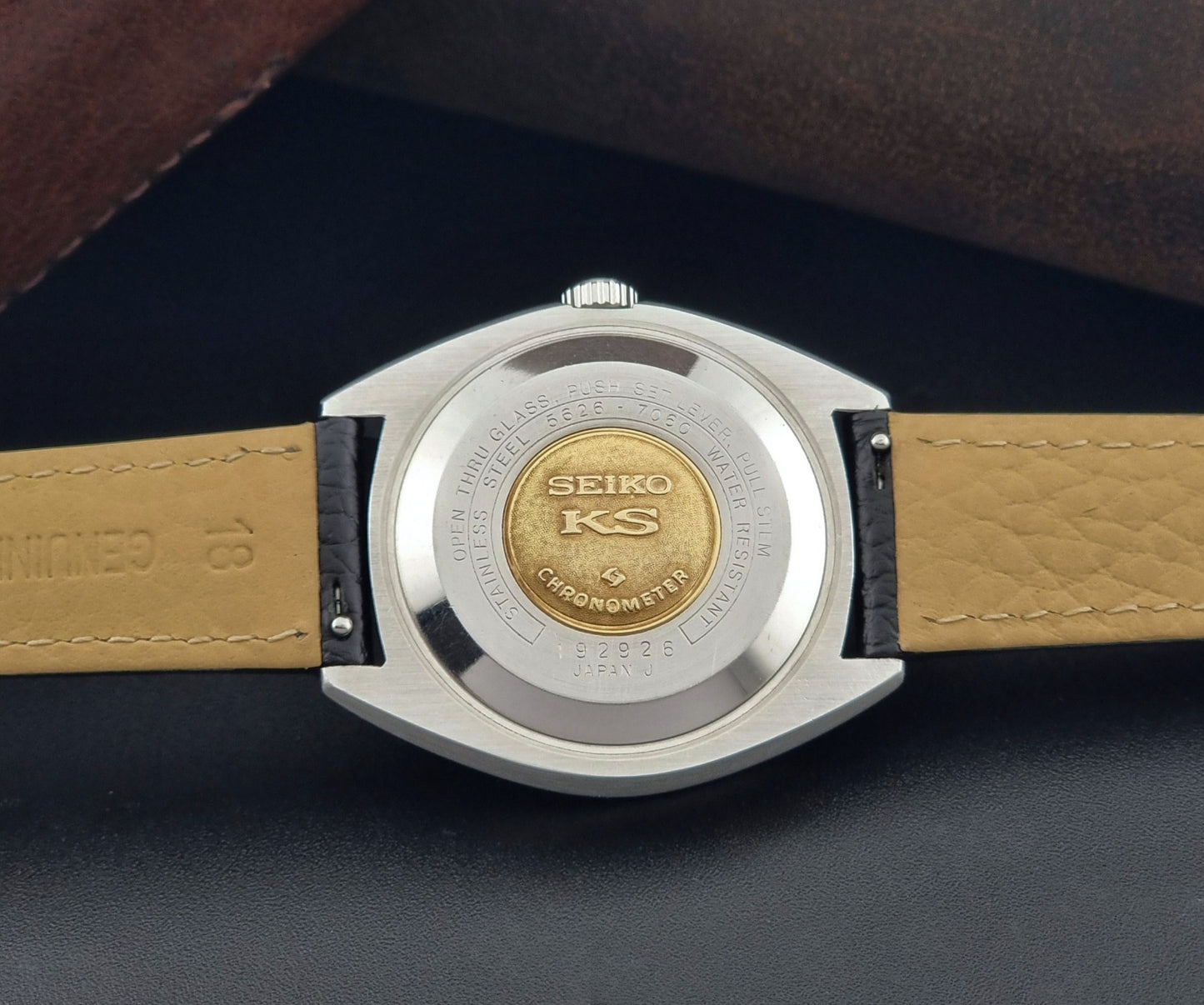 Vintage King Seiko 5626-7060 wristwatch with a silver case and black leather strap on a dark surface case back view