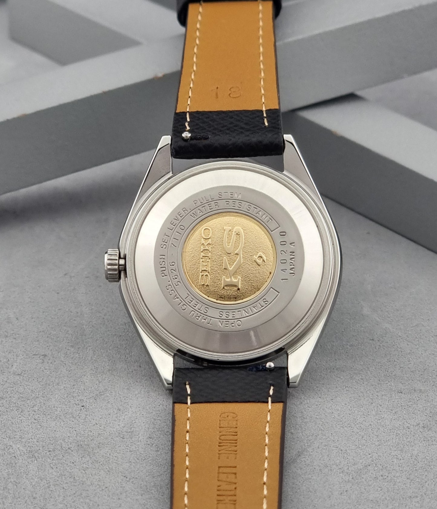 Vintage King Seiko Wristwatch 5626-7110 with a silver case and black strap on a dark gray background case back view