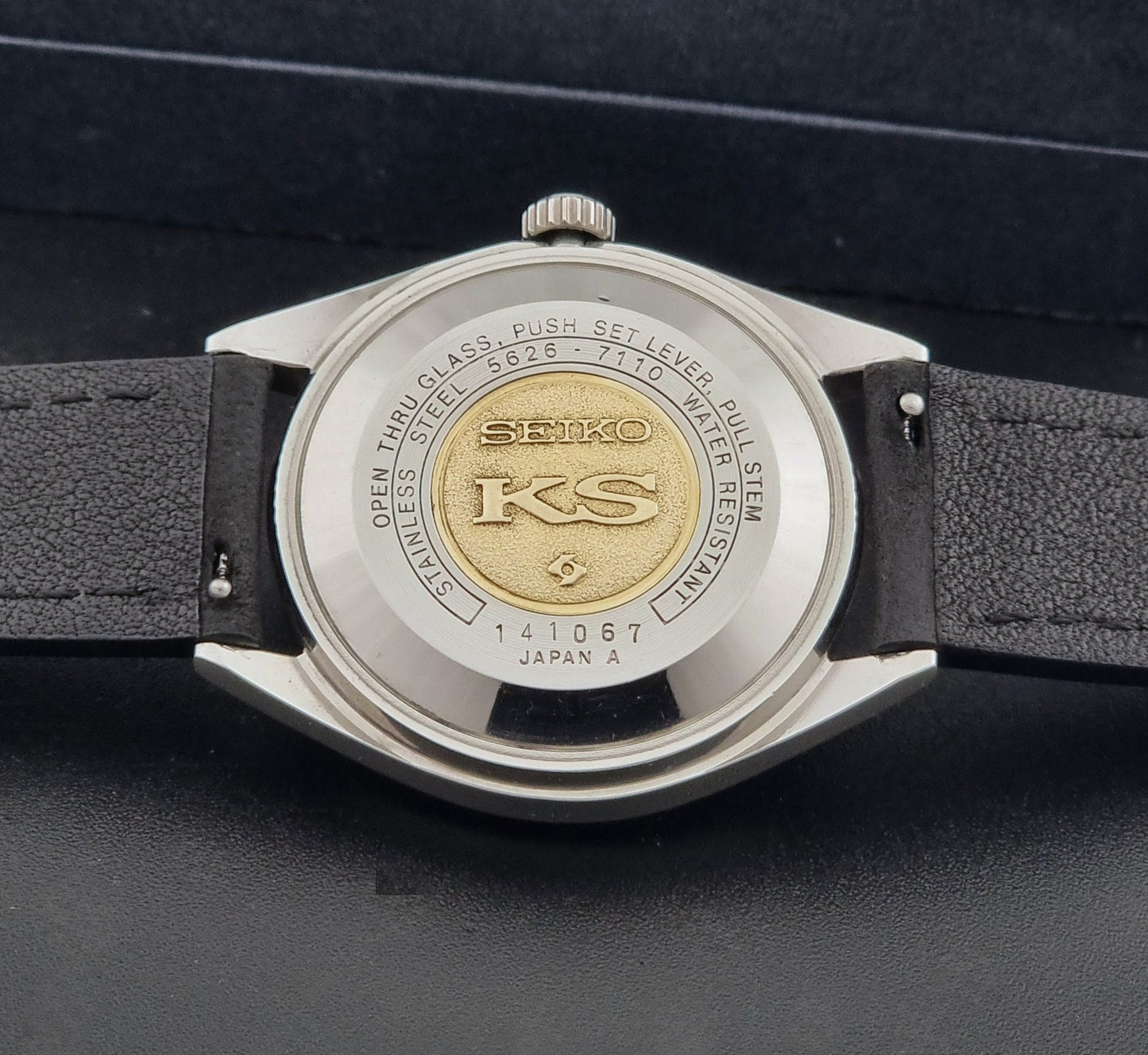 Vintage King Seiko 5626-7110 wristwatch with black leather strap on a gray background case back view
