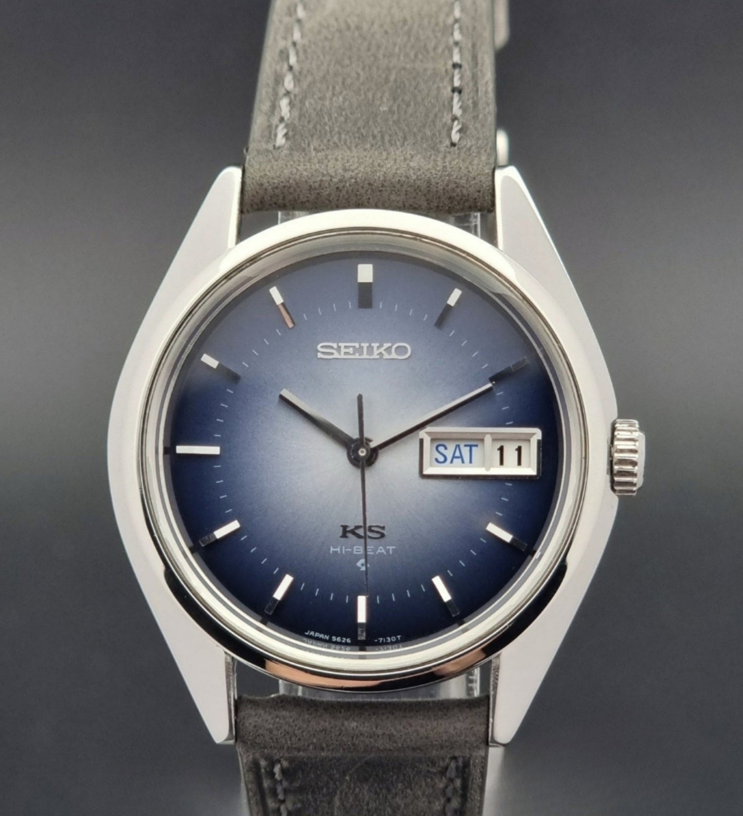 Vintage King Seiko Wristwatch 5626-7111 with a blue dial and gray leather strap on a textured dark background close up front