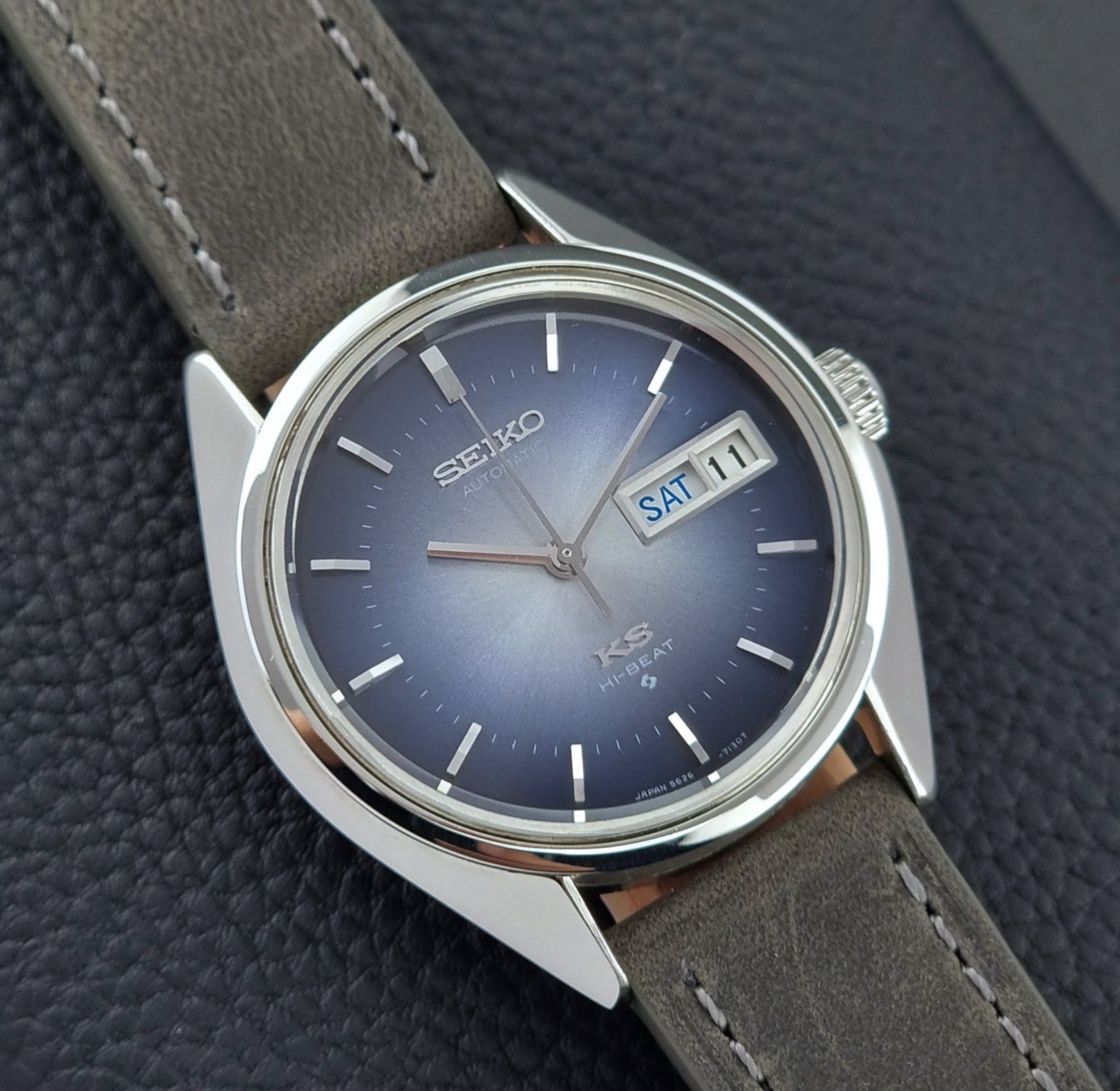 Vintage King Seiko Wristwatch 5626-7111 with a blue dial and gray leather strap on a textured dark background close up of the dial