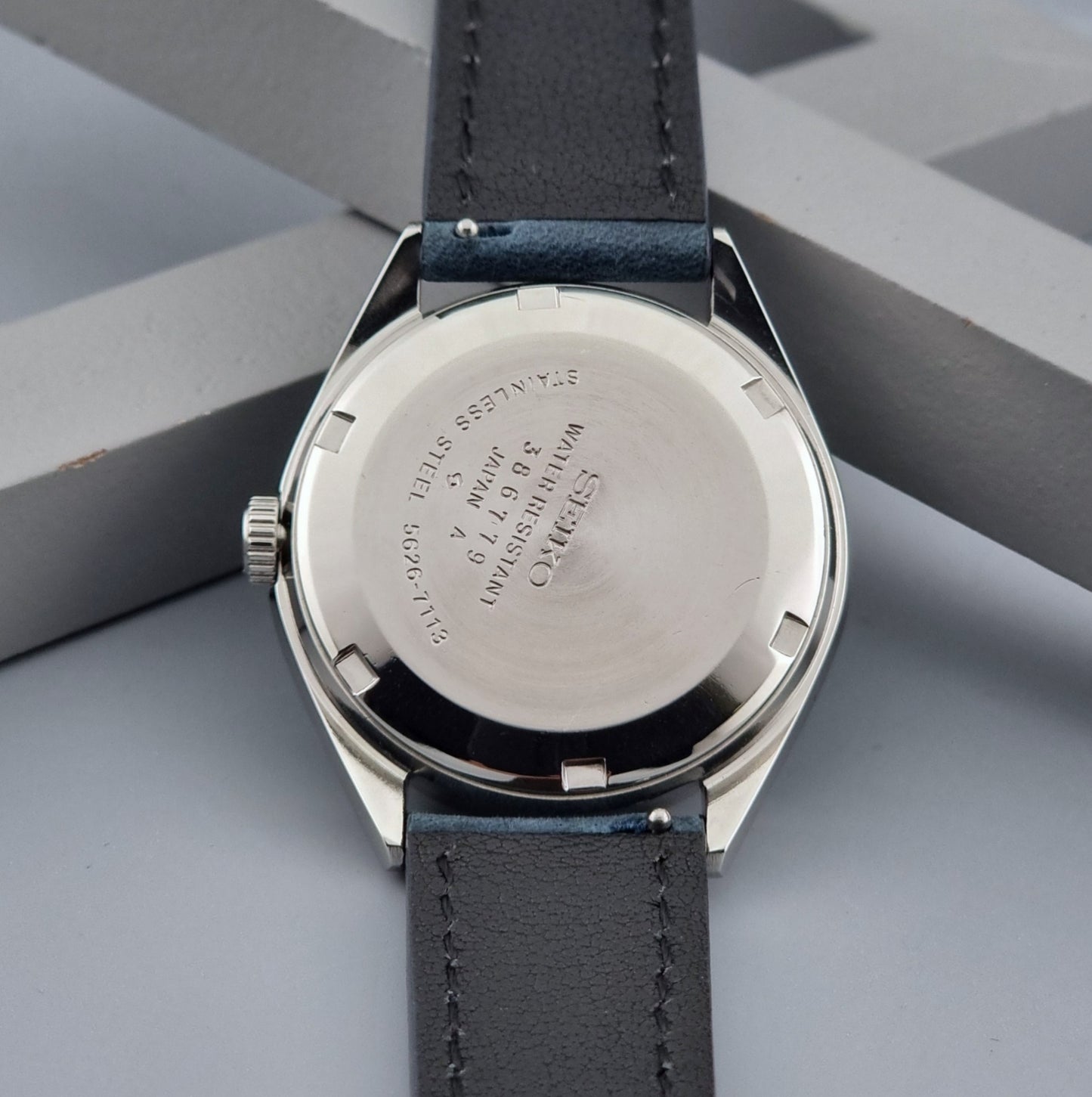 Vintage King Seiko wristwatch with a blue strap on a gray background case back view