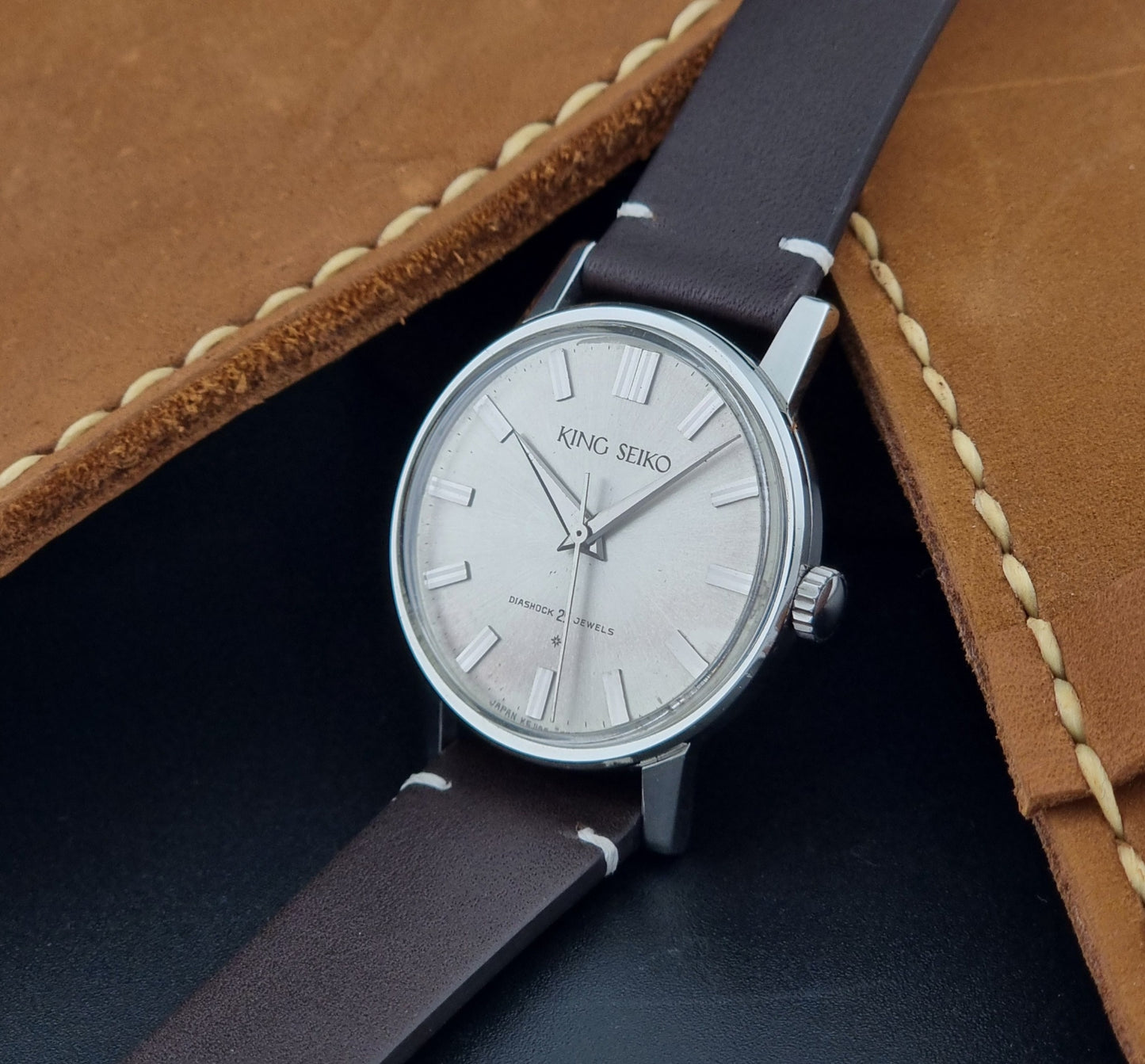 Vintage King Seiko J14102E Wristwatch with brown leather strap on a dark gray background crown view