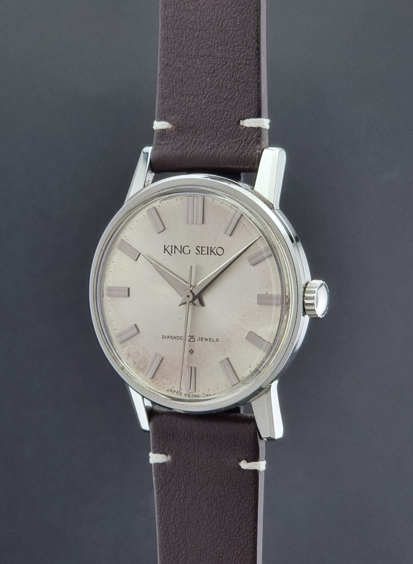 Vintage King Seiko J14102E Wristwatch with brown leather strap on a dark gray background crown profile