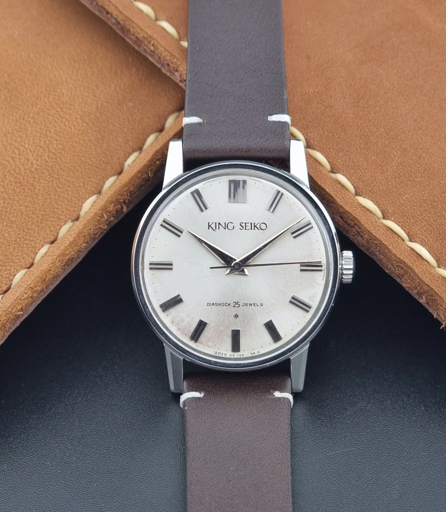 Vintage King Seiko J14102E Wristwatch with brown leather strap on a dark gray background front view