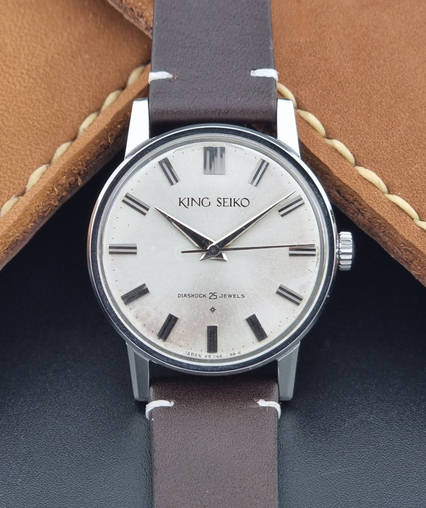 Vintage King Seiko J14102E Wristwatch with brown leather strap on a dark gray background close up dial