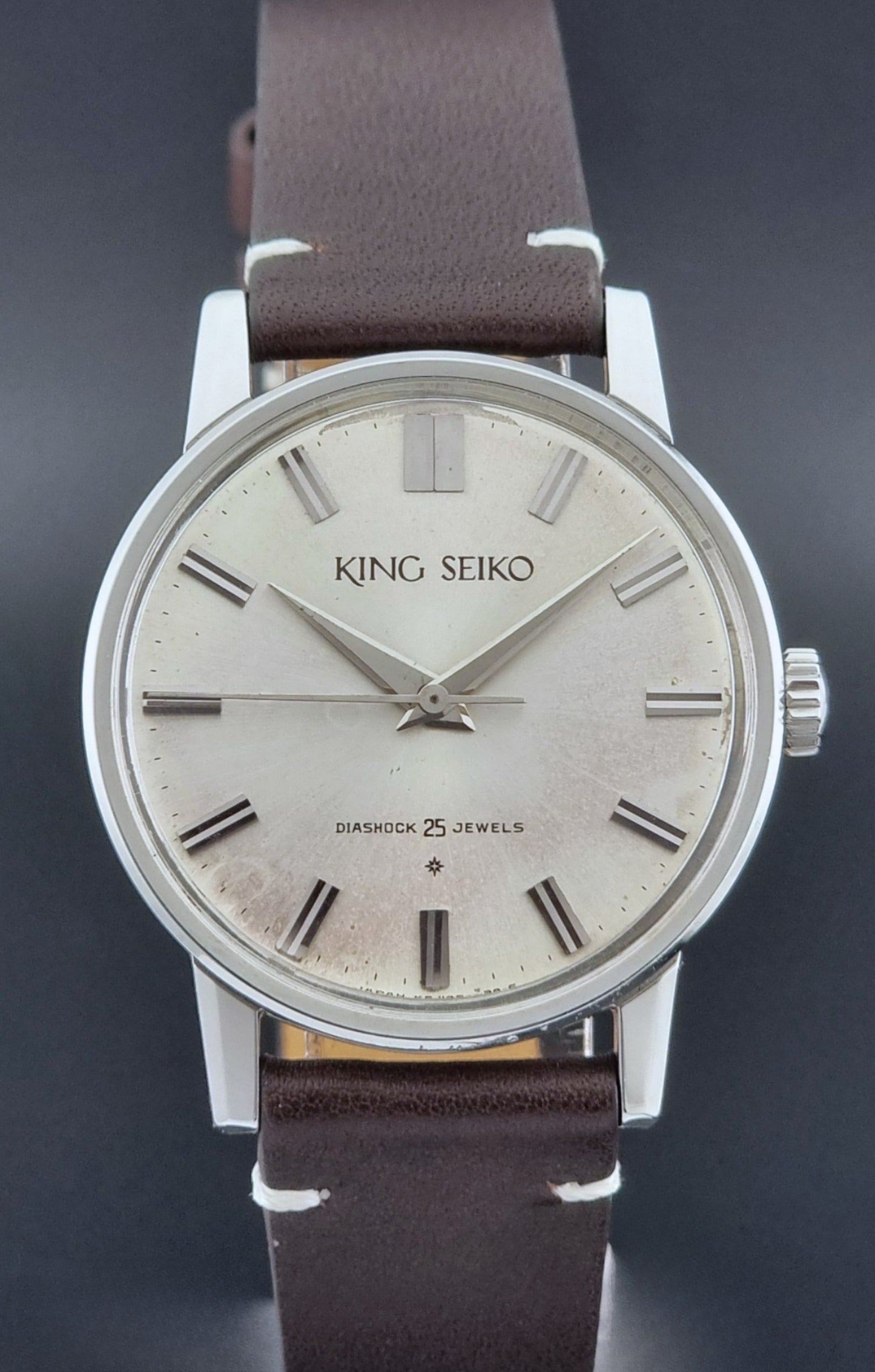 Vintage King Seiko J14102E Wristwatch with brown leather strap on a dark gray background close up
