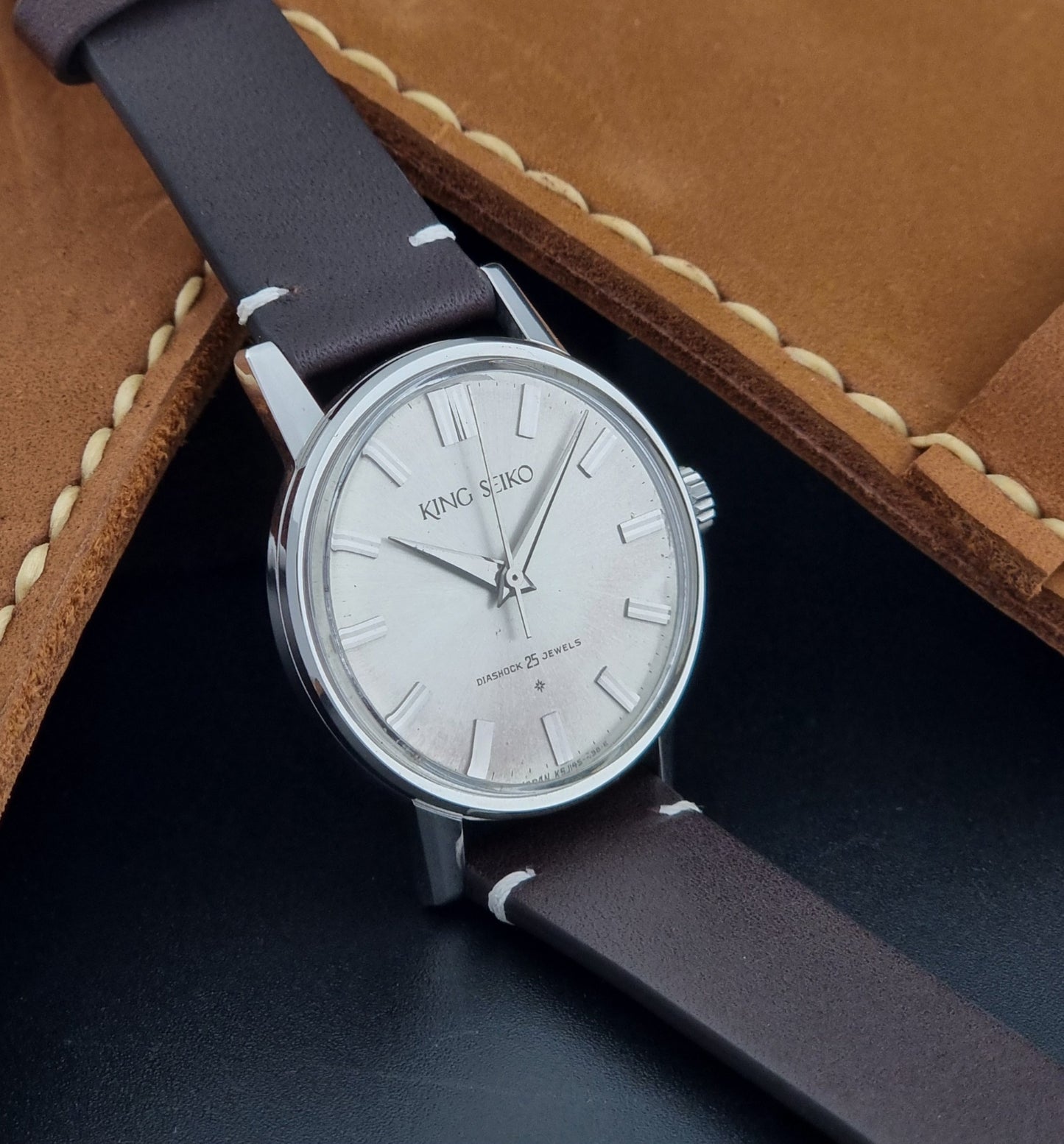 Vintage King Seiko J14102E Wristwatch with brown leather strap on a dark gray background sideview