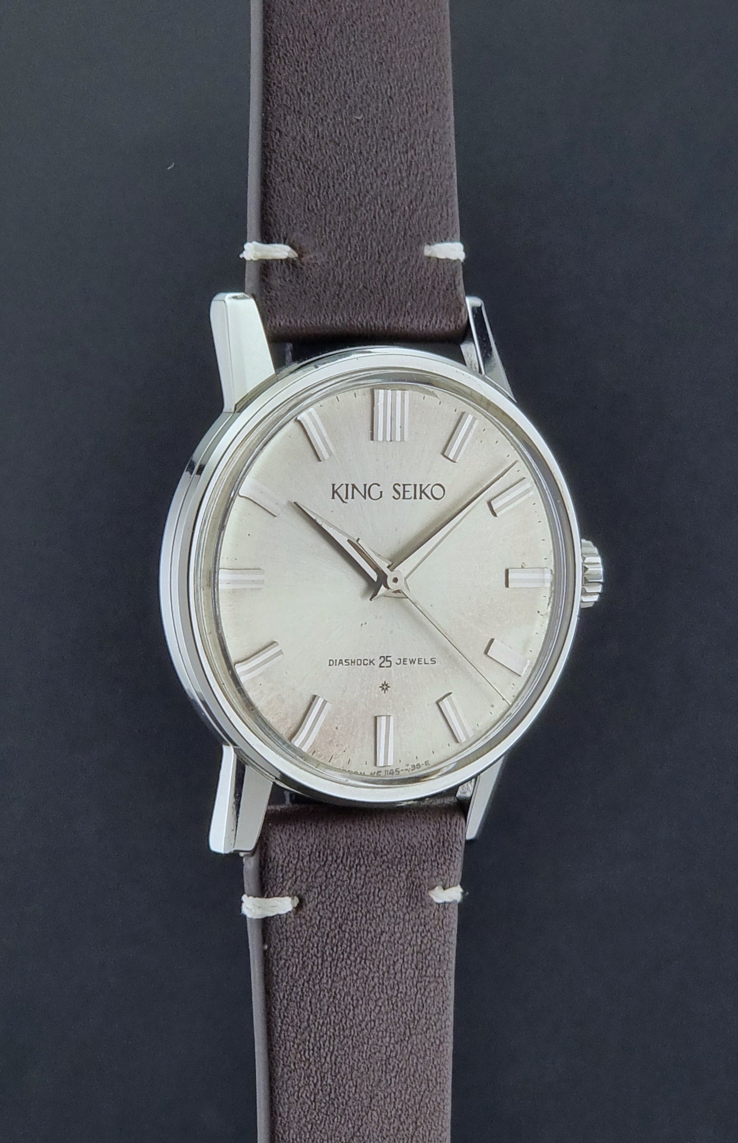 Vintage King Seiko J14102E Wristwatch with brown leather strap on a dark gray background side profile